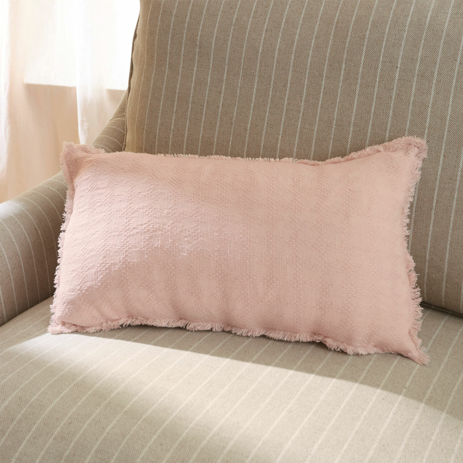 Roze sierkussen van zachte stof op beige gestreepte bank voor een gezellige woonkamer