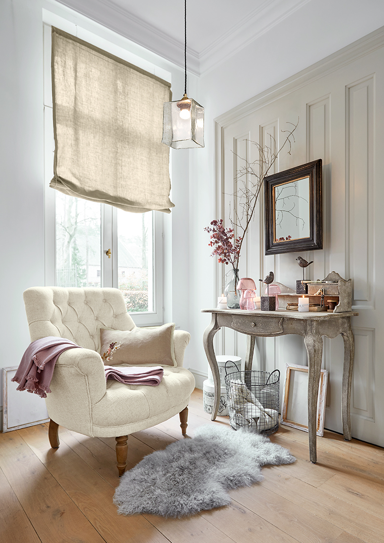 Comfortabele crèmekleurige fauteuil met gestikte rug en houten poten in lichte woonkamer met vloerkleed en sidetable