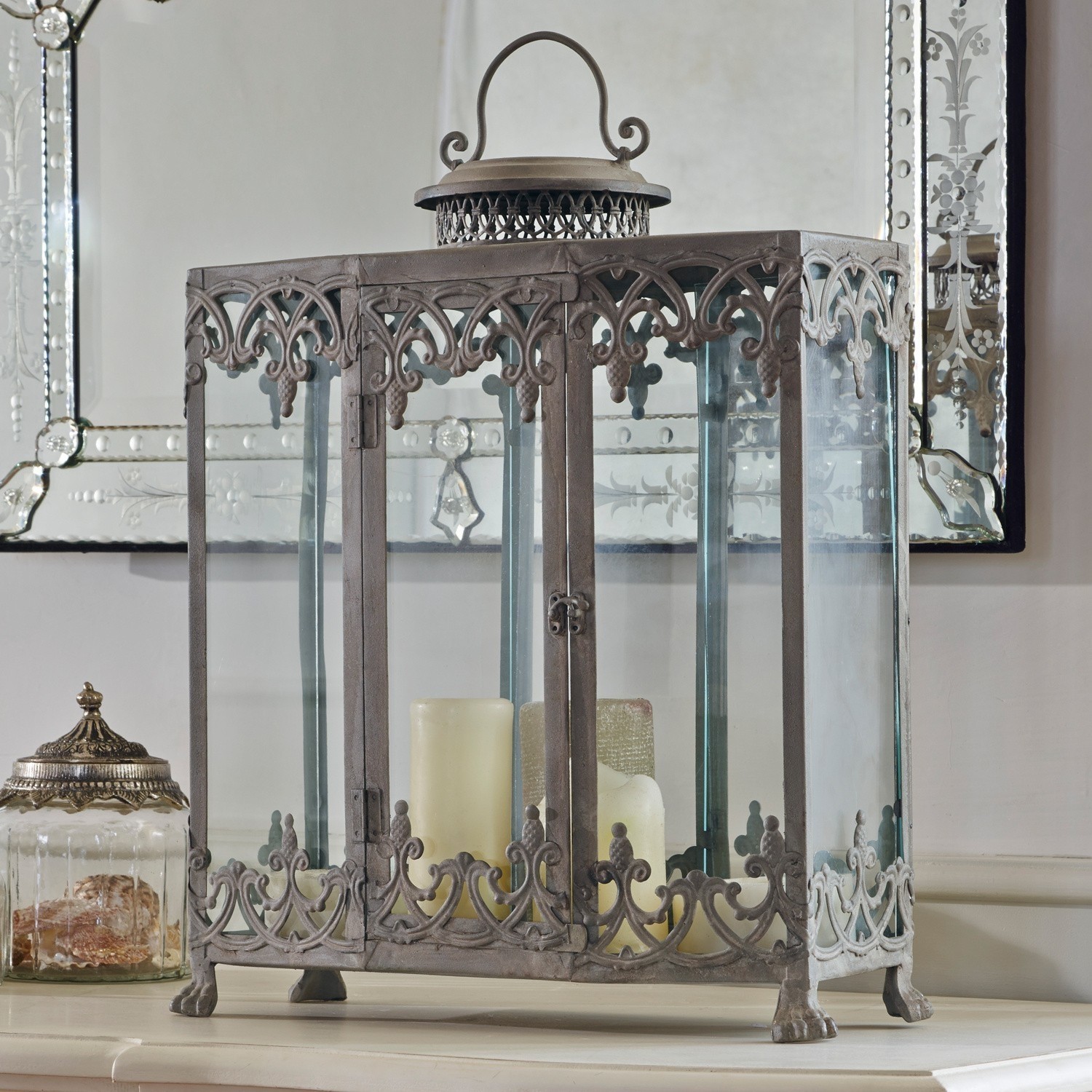 Lanterne décorative en métal avec panneaux en verre et bougies crème posée sur une table