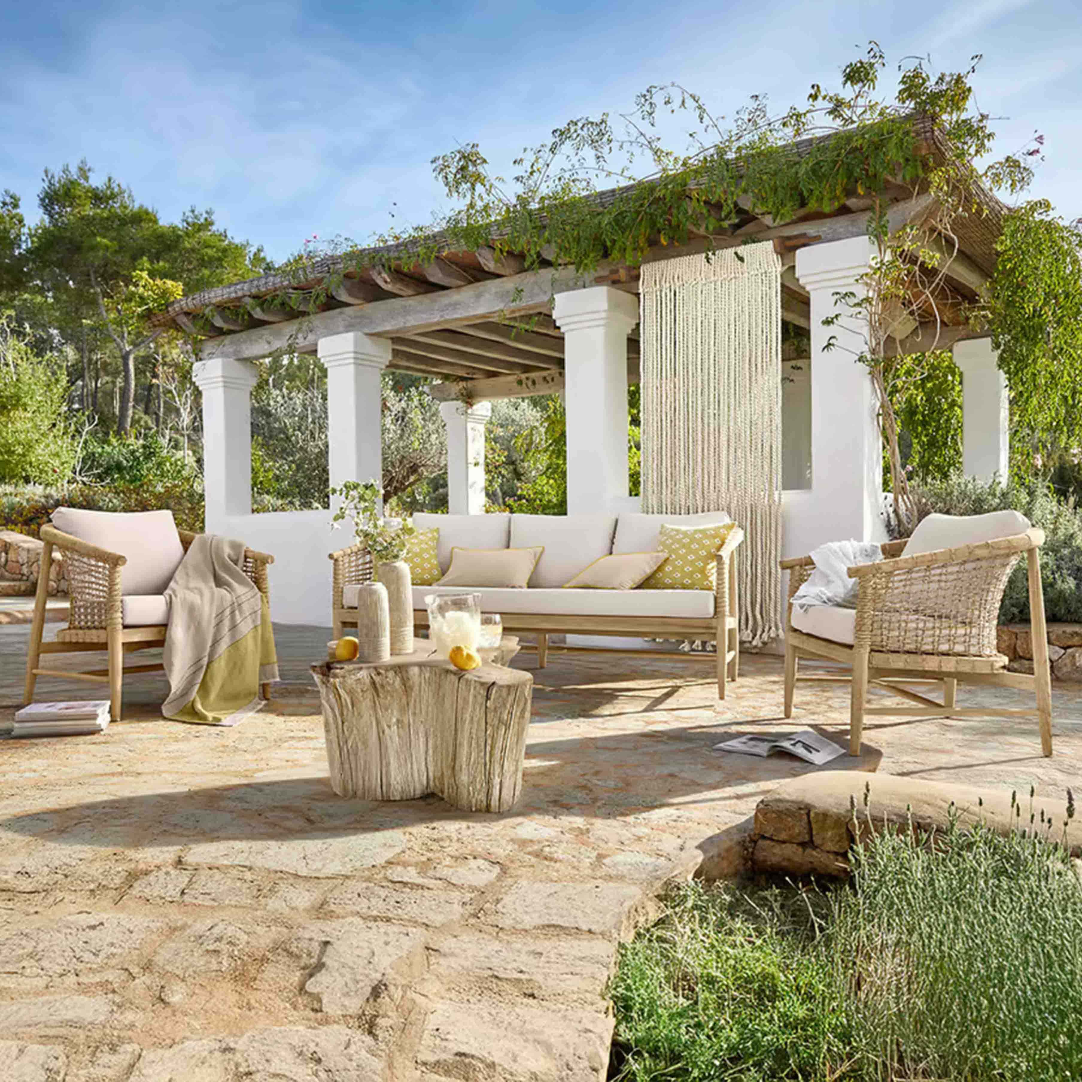Ensemble de mobilier de jardin en bois clair avec coussins beige sur patio en pierre sous une pergola végétalisée