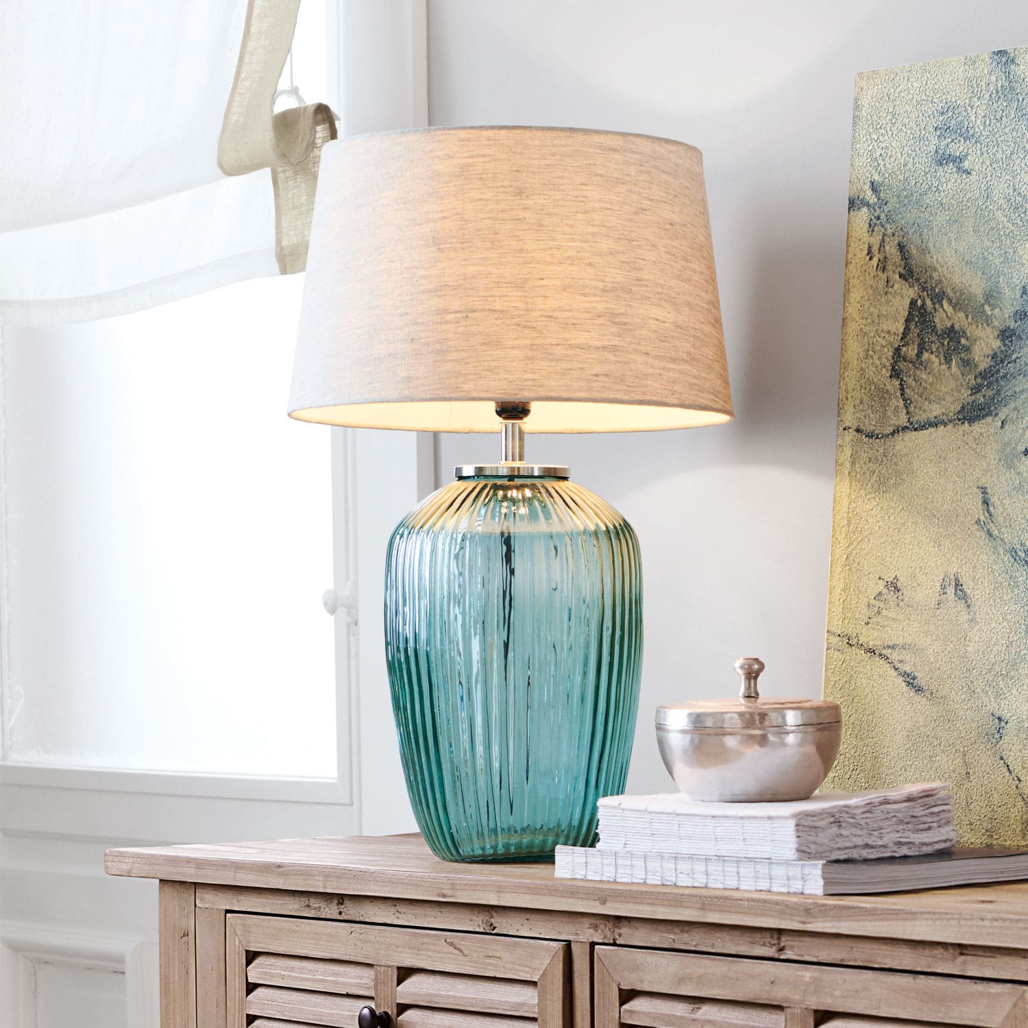 Lampe à poser Fenis Lampe de table en verre vert avec abat-jour beige posée sur un meuble en bois clair