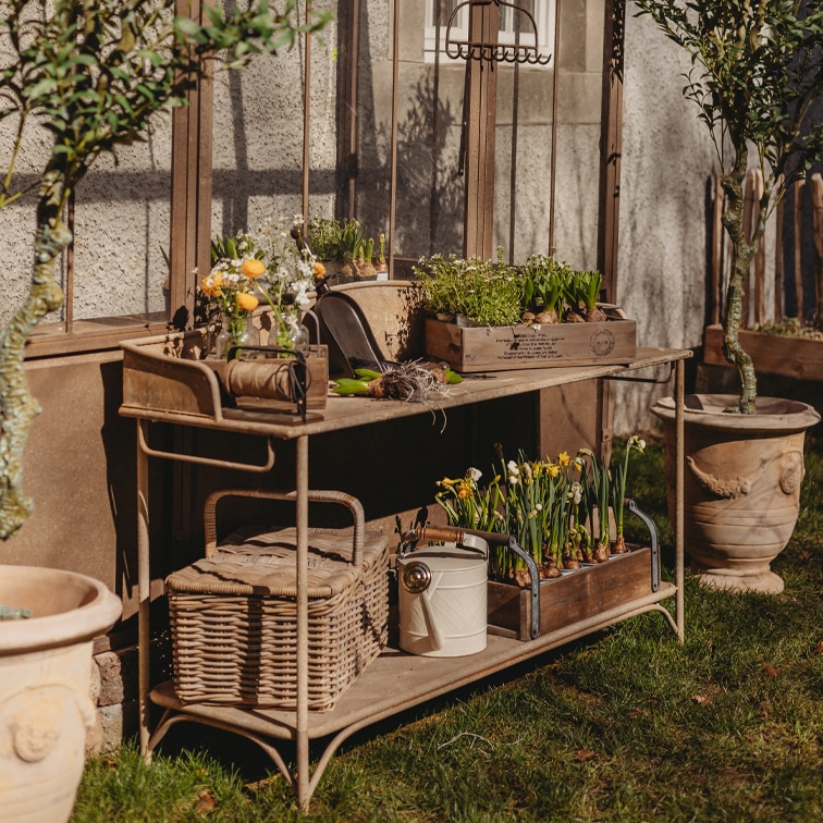 Metalen tuintafel met houten kisten en bloempotten op gras bij een kasmuur