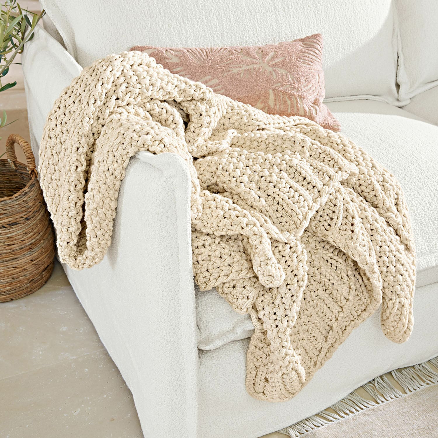 Plaid Plixoren Plaid beige épais en coton tricoté à la main sur un canapé blanc dans un intérieur lumineux