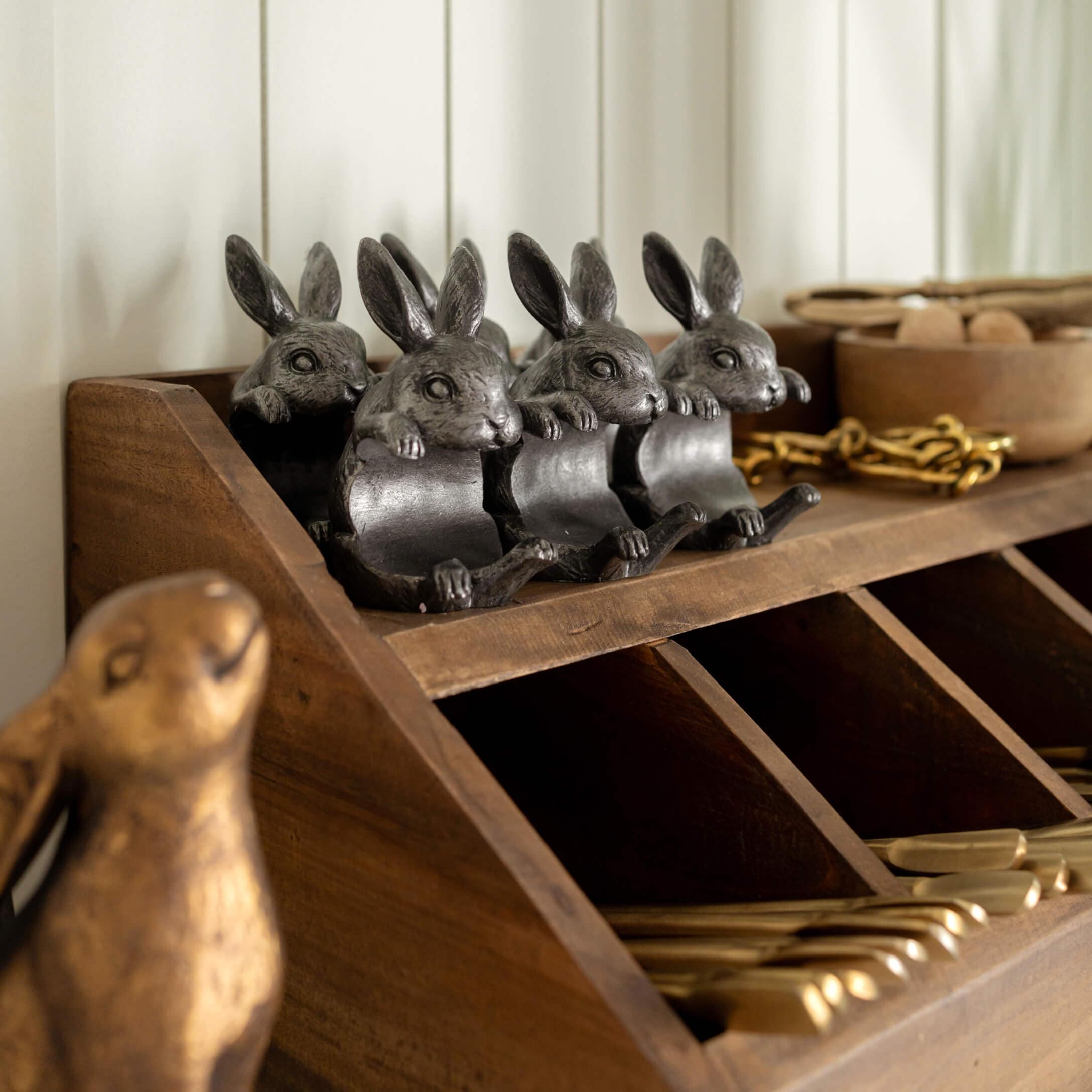Quatre décorations lapin en métal gris foncé posées sur une étagère en bois avec compartiments