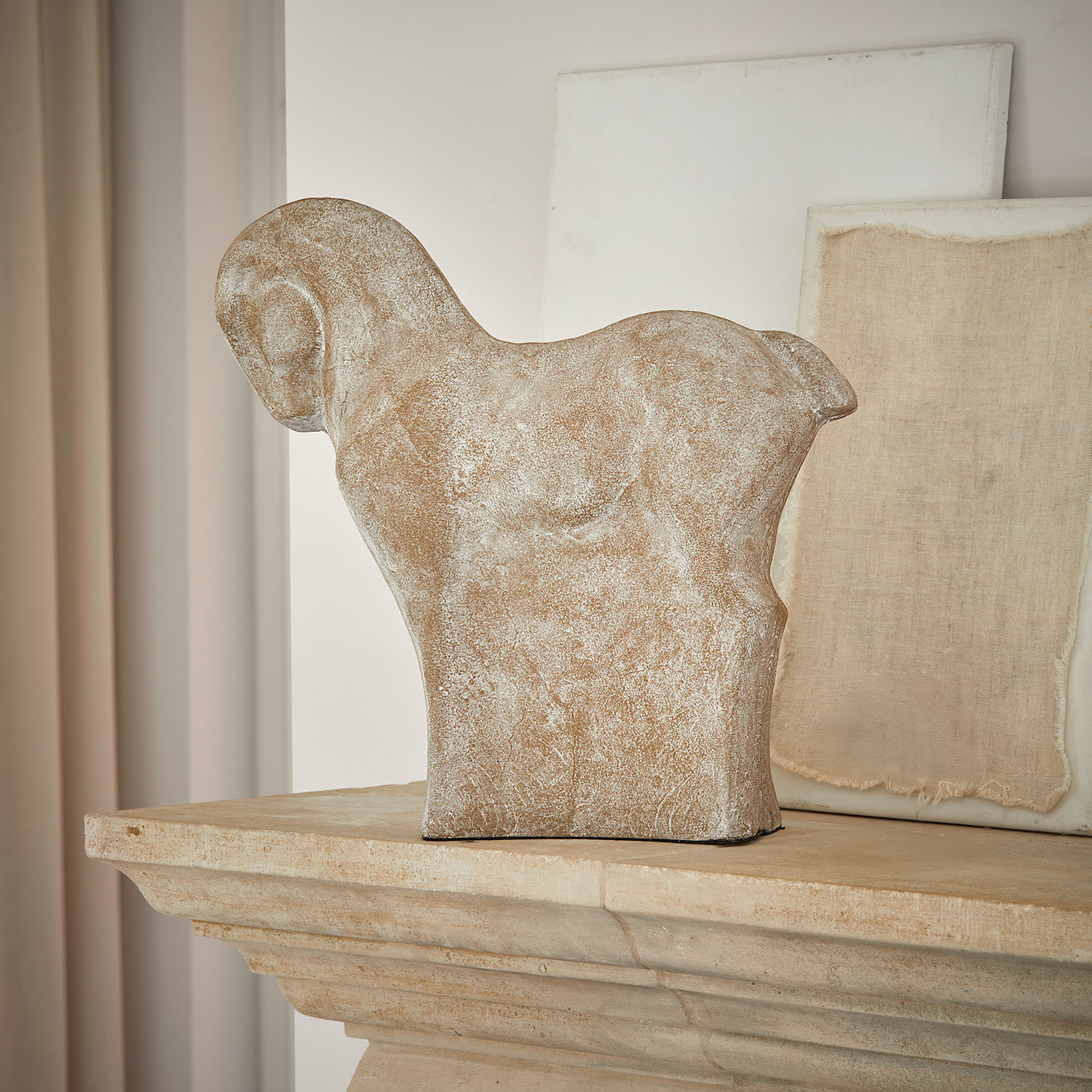 Sculpture décorative de cheval en pierre beige posée sur une cheminée en pierre rustique