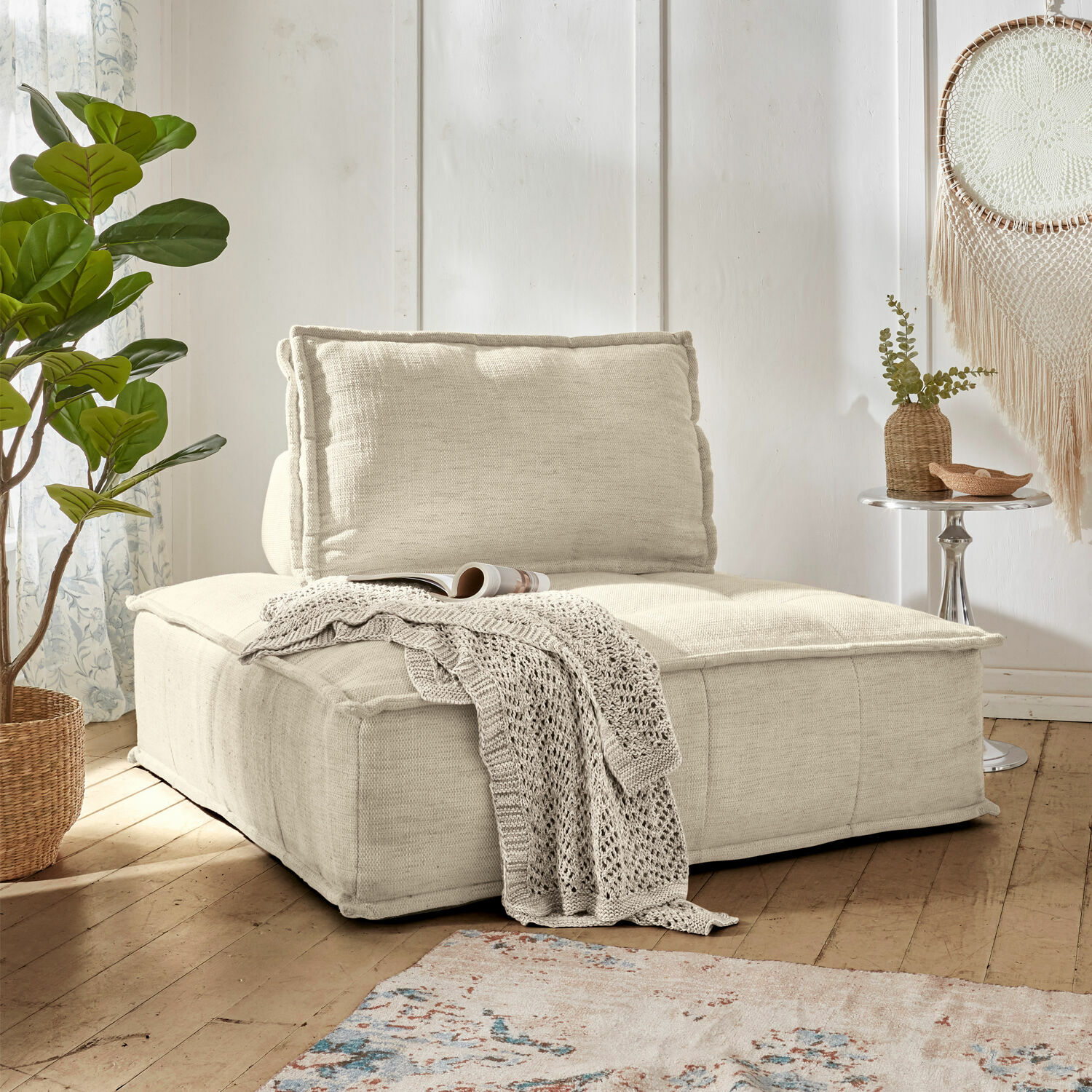 Loungebank Tesshill Beige stoffen fauteuil met zachte rugleuning en gebreide deken in lichte woonkamer met houten vloer