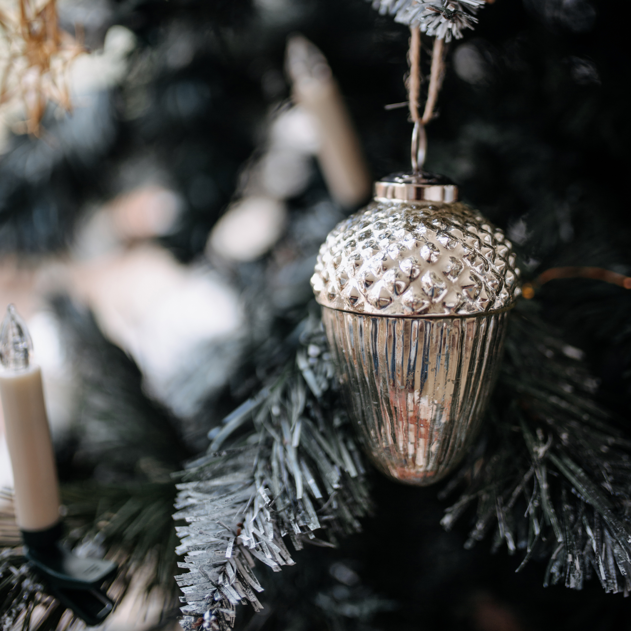 Décoration de Noël argentée en forme de gland avec texture, suspendue à un sapin vert