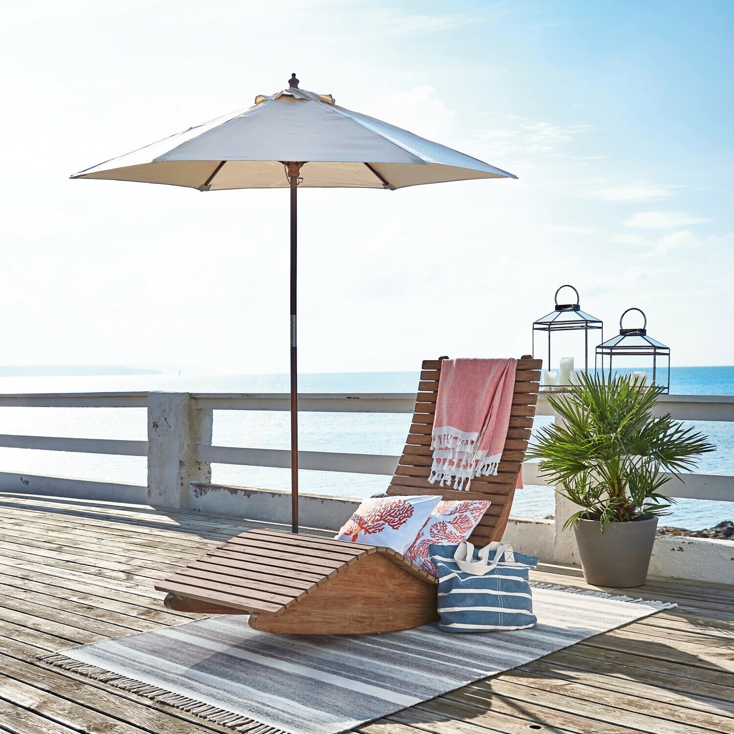 Parasol Enfield Chaise longue en bois avec parasol blanc et coussins décoratifs sur terrasse ensoleillée au bord de la mer
