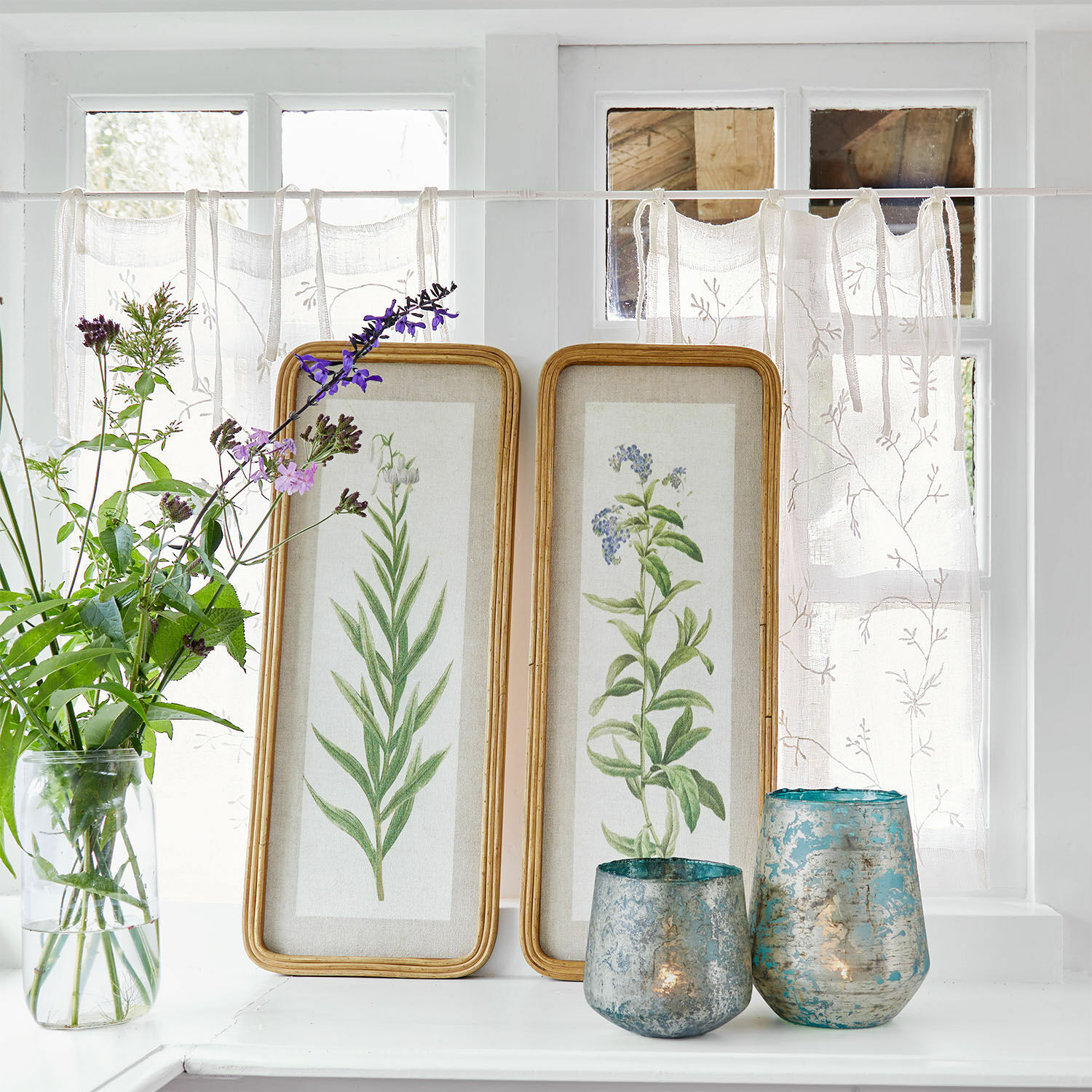 Lot de 2 tableaux Cenori Deux cadres en bois avec illustrations botaniques posés sur un rebord blanc avec bougeoirs décoratifs bleus