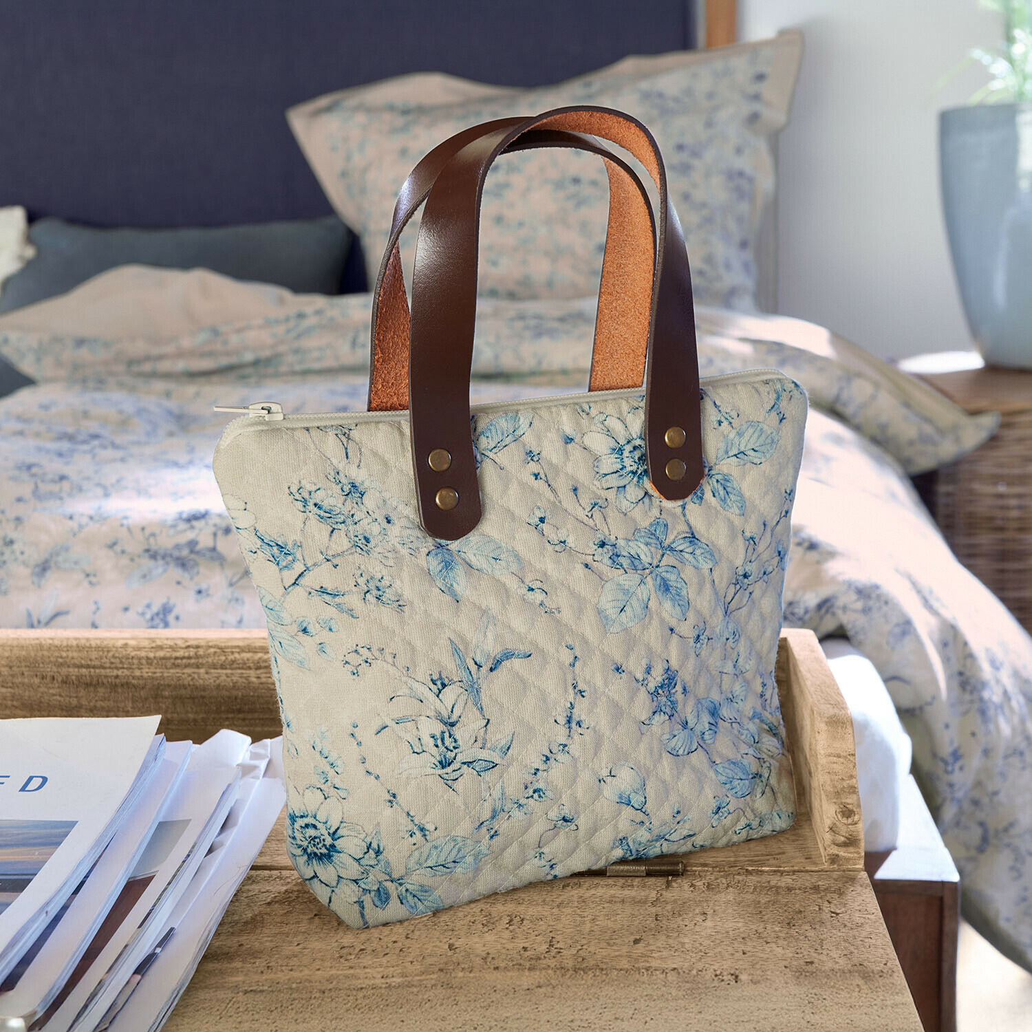 Tas Vailenne Beige gewatteerde tas met blauw bloemenpatroon en bruine leren handvatten op houten tafel