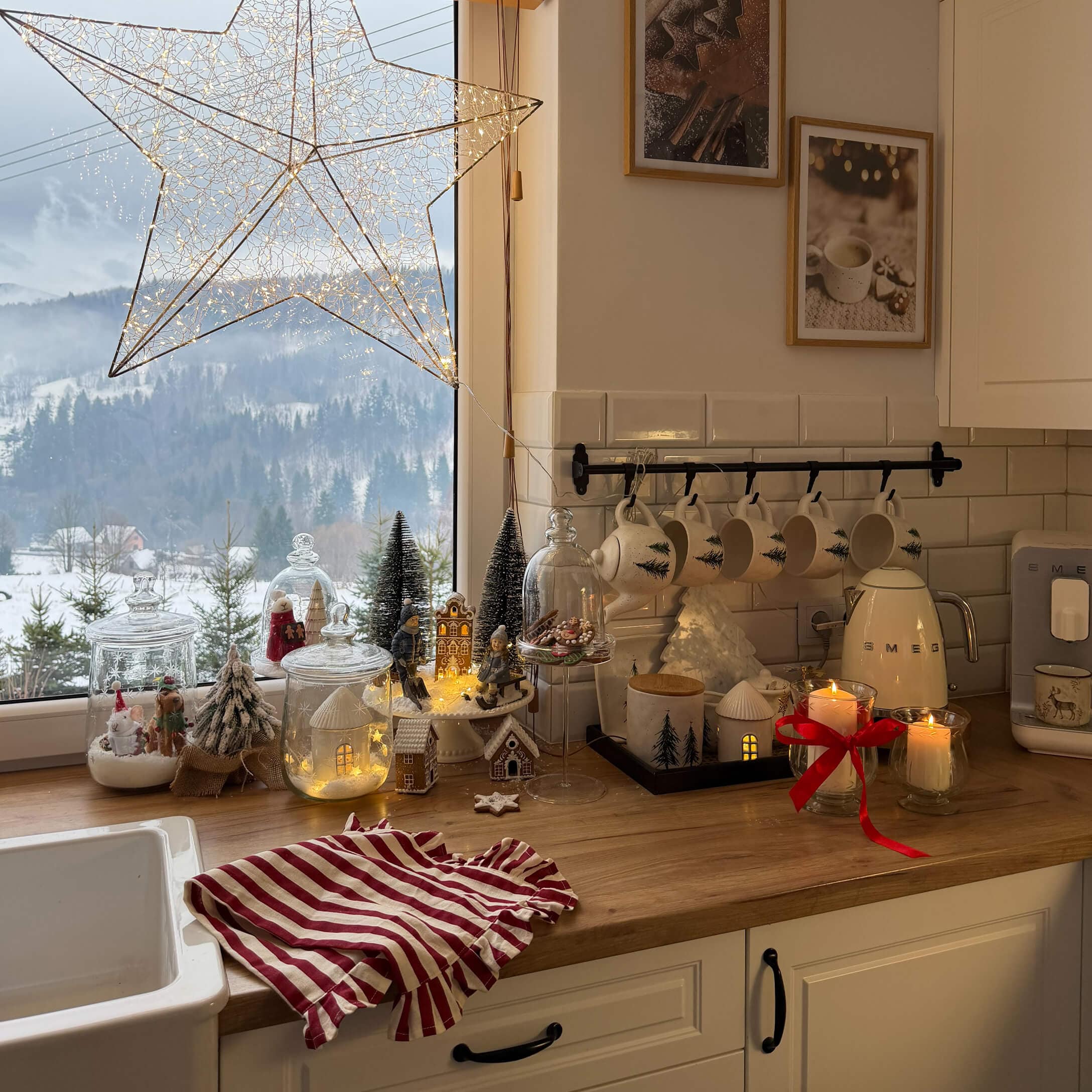 Cuisine avec plan de travail en bois décoré pour Noël, tasses blanches à motif sapin et guirlandes lumineuses
