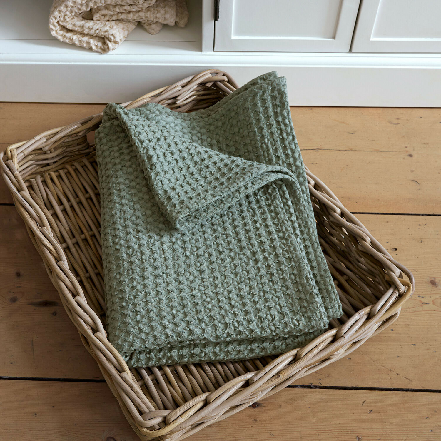 Badhanddoek Maralei Zachte groene katoenen deken met wafelstructuur in een rieten mand op een houten vloer
