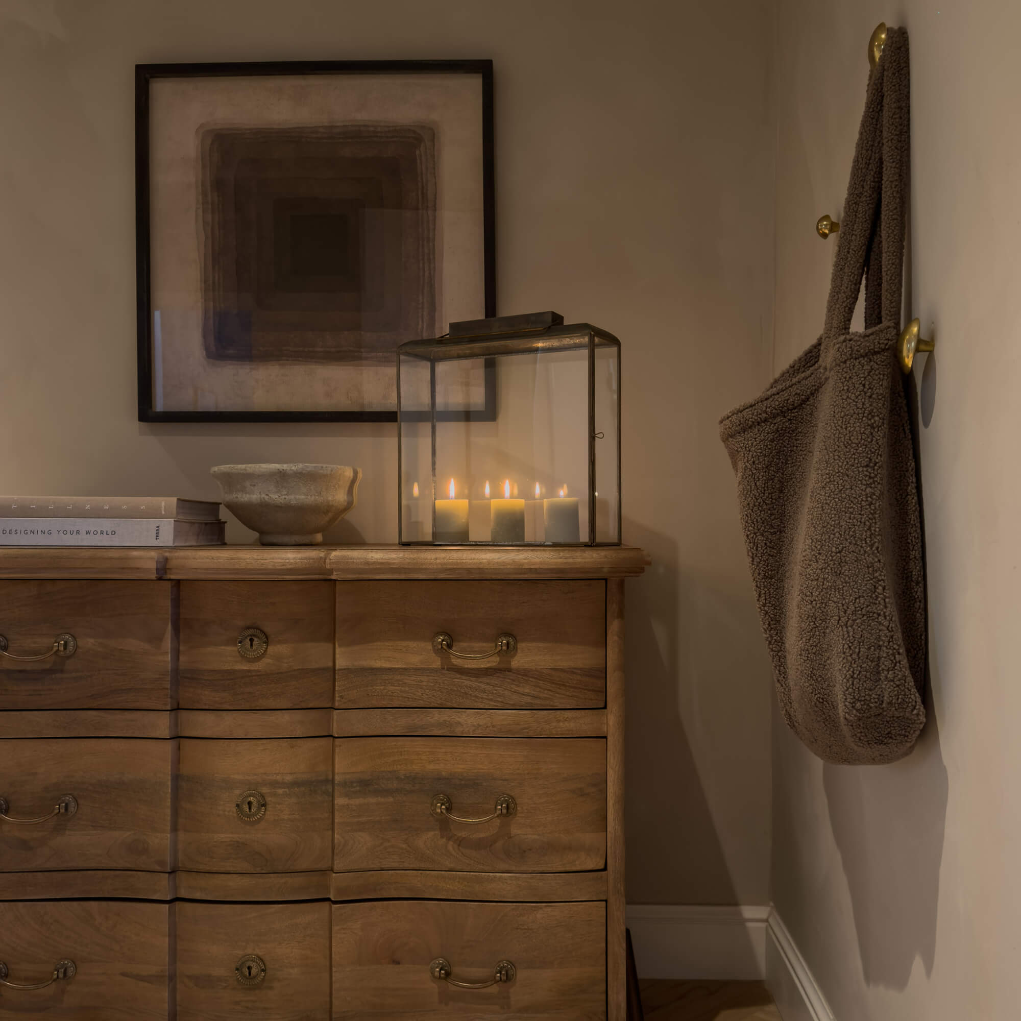 Commode en bois avec poignées en laiton, bougeoir en verre et sac marron doux accroché au mur