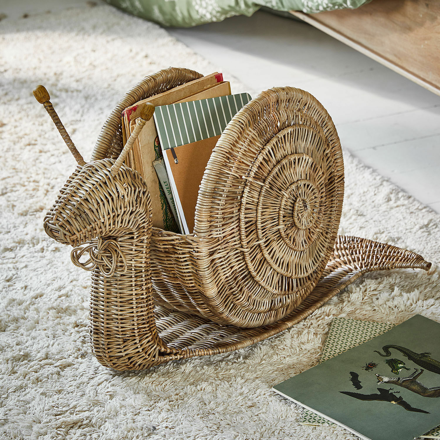 Corbeille Tigrelle Porte-livres en forme d'escargot en osier naturel posé sur un tapis moelleux blanc cassé