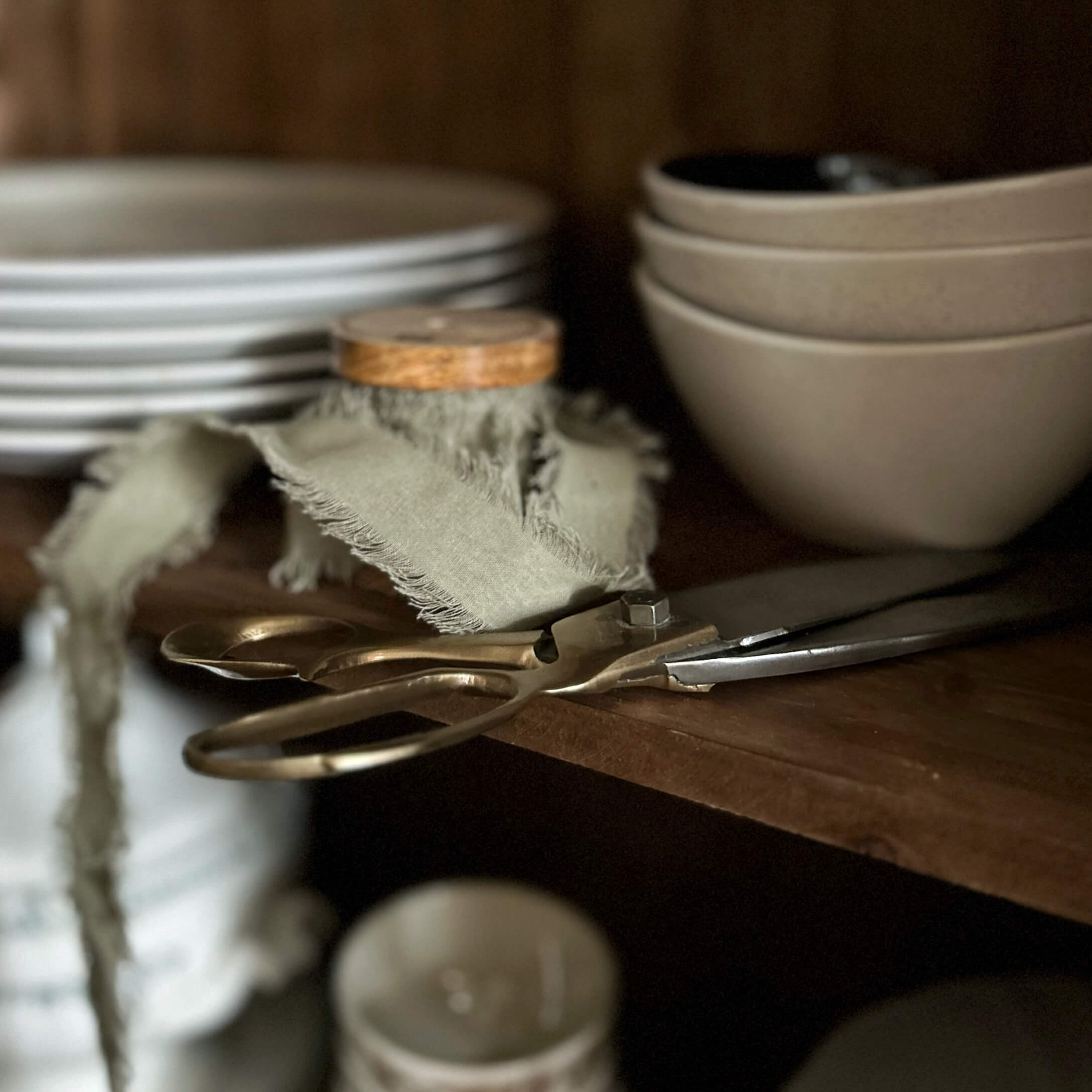 Oude messing schaar op houten plank naast beige kommen en borden in keuken