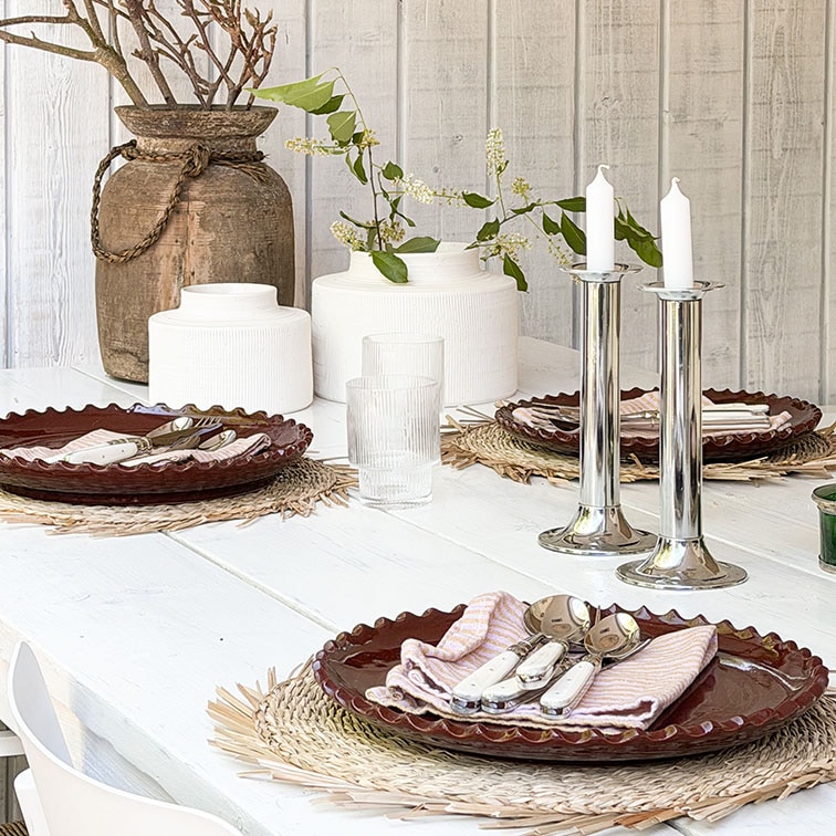 Table en bois blanc avec assiettes en céramique brunes et bougeoirs argentés sur sets décoratifs