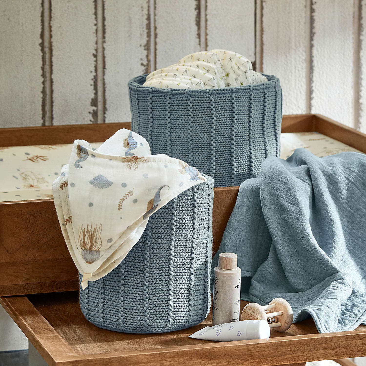 Mand set van 2 Fiorenzo Twee blauwe gebreide manden voor luiers en babyspullen op een houten commode