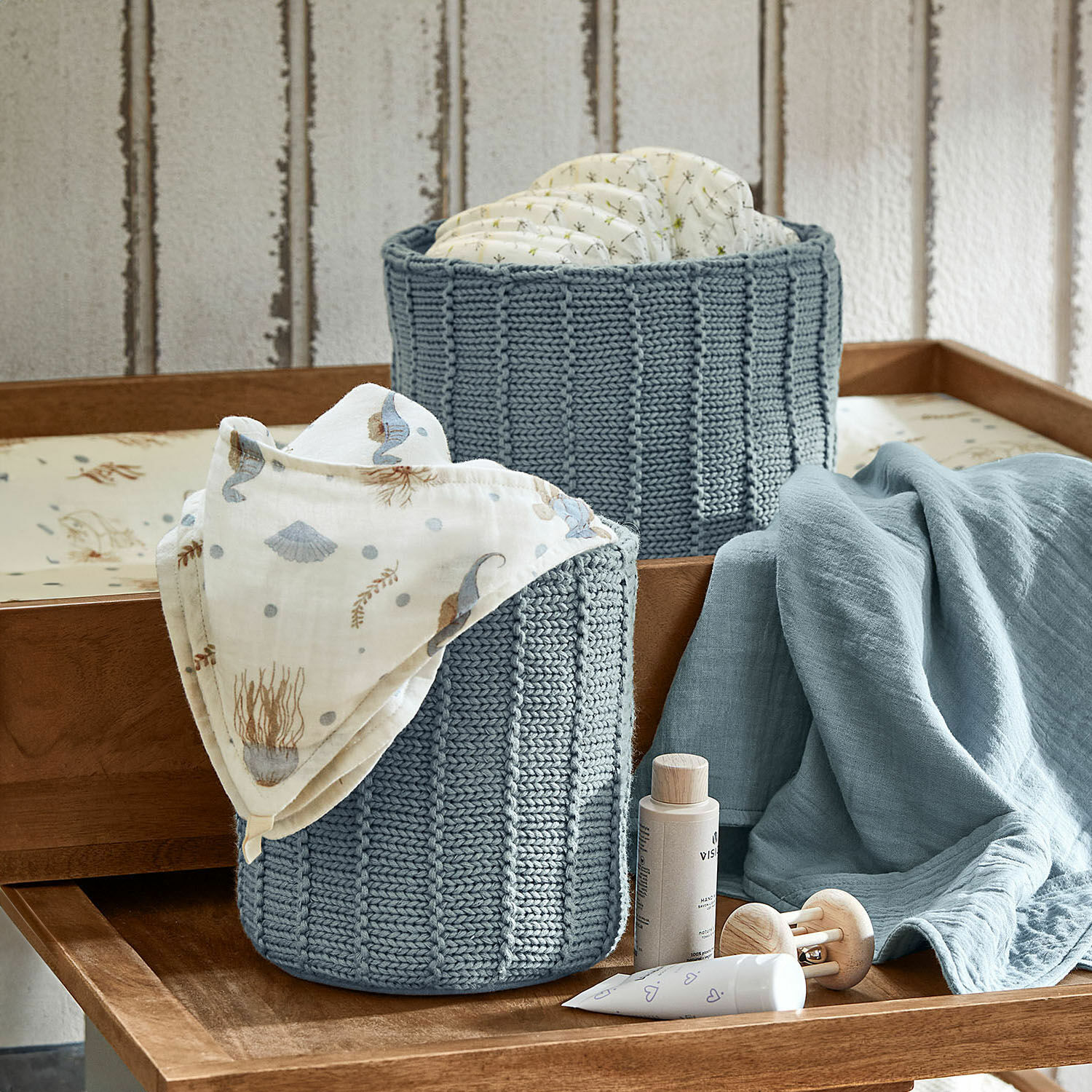Mand set van 2 Fiorenzo Twee blauwe gebreide manden voor luiers en babyspullen op een houten commode