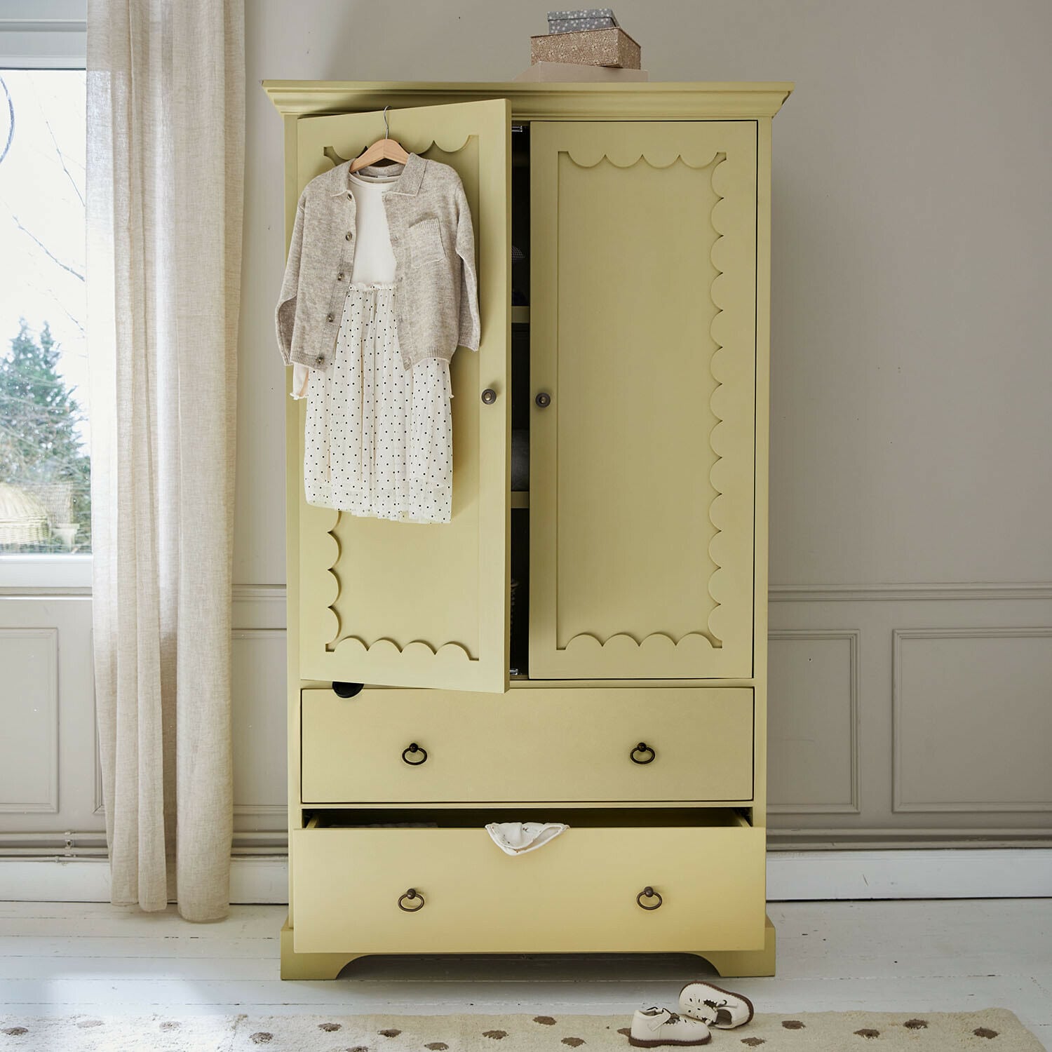 Armoire pour enfant Frollin Armoire en bois jaune avec portes décoratives et vêtements d'enfant suspendus dans une pièce lumineuse