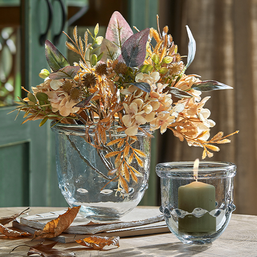 Glazen vaas met gedroogde bloemen in beige en bruine tinten en windlicht met kaars op houten tafel