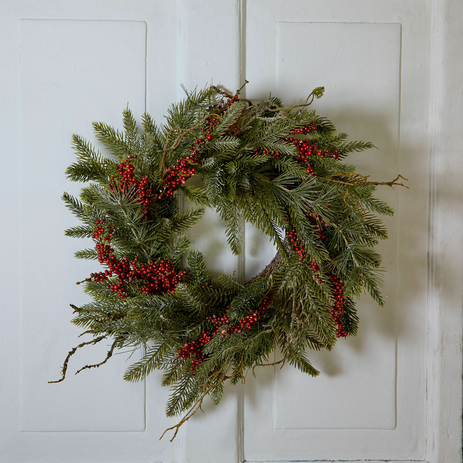 Couronne Zenzola Couronne de Noël en branches vertes et baies rouges accrochée à une porte blanche, décoration festive