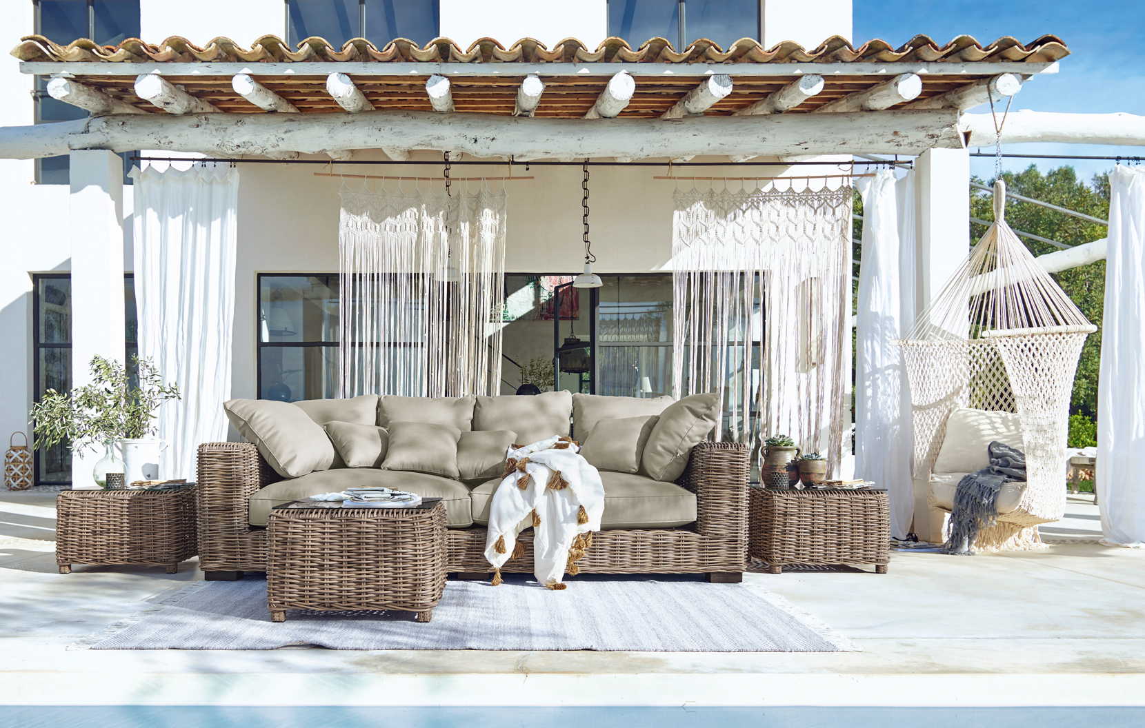 Ensemble de meubles de jardin en osier avec coussins beige sur terrasse avec hamac et décor bohème