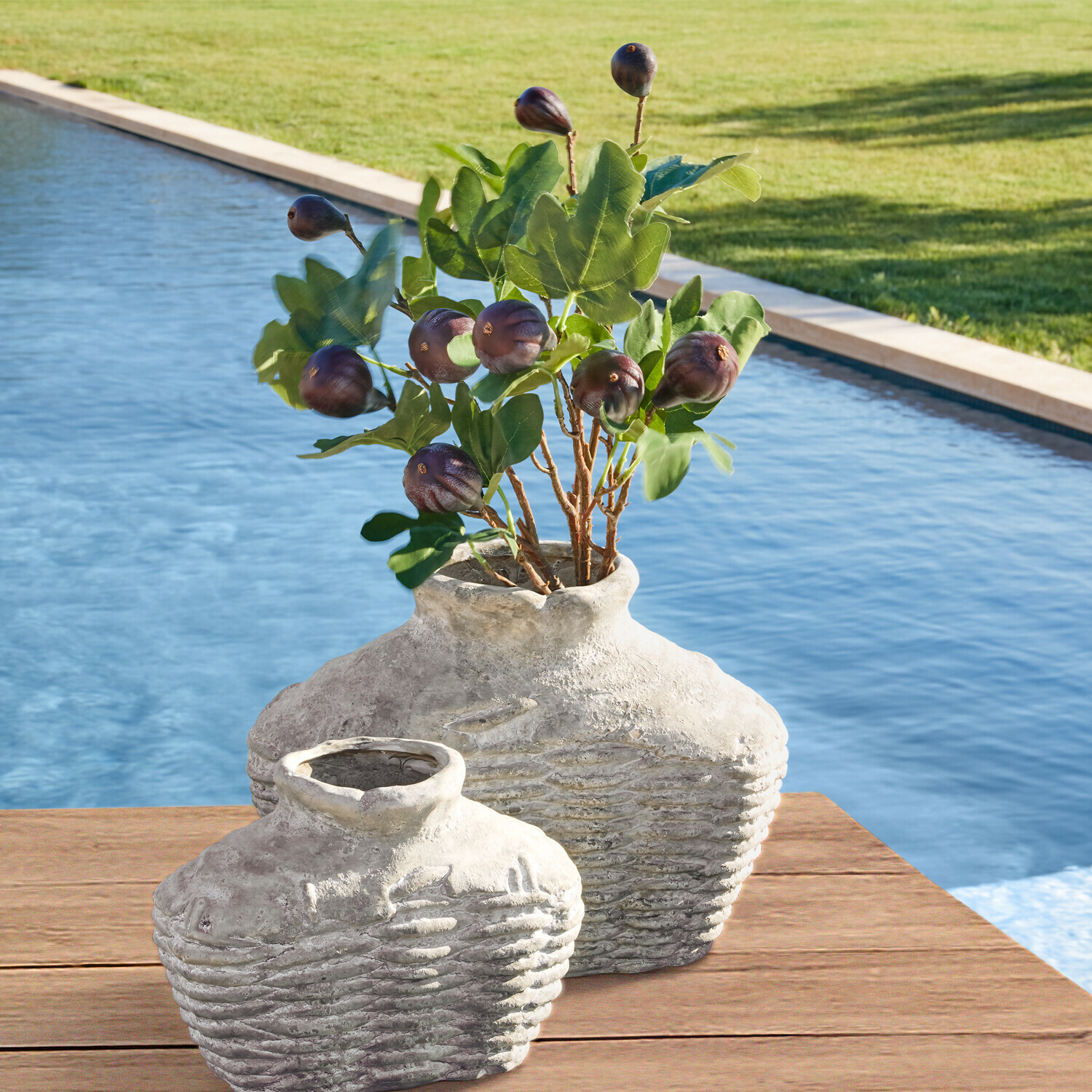 Deux vases rustiques en céramique grise sur une table en bois près de la piscine avec feuillage vert et fruits
