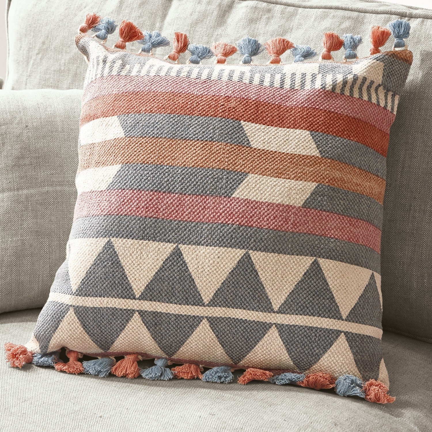 Coussin décoratif en coton avec motifs géométriques et pompons bleus et orange sur canapé clair