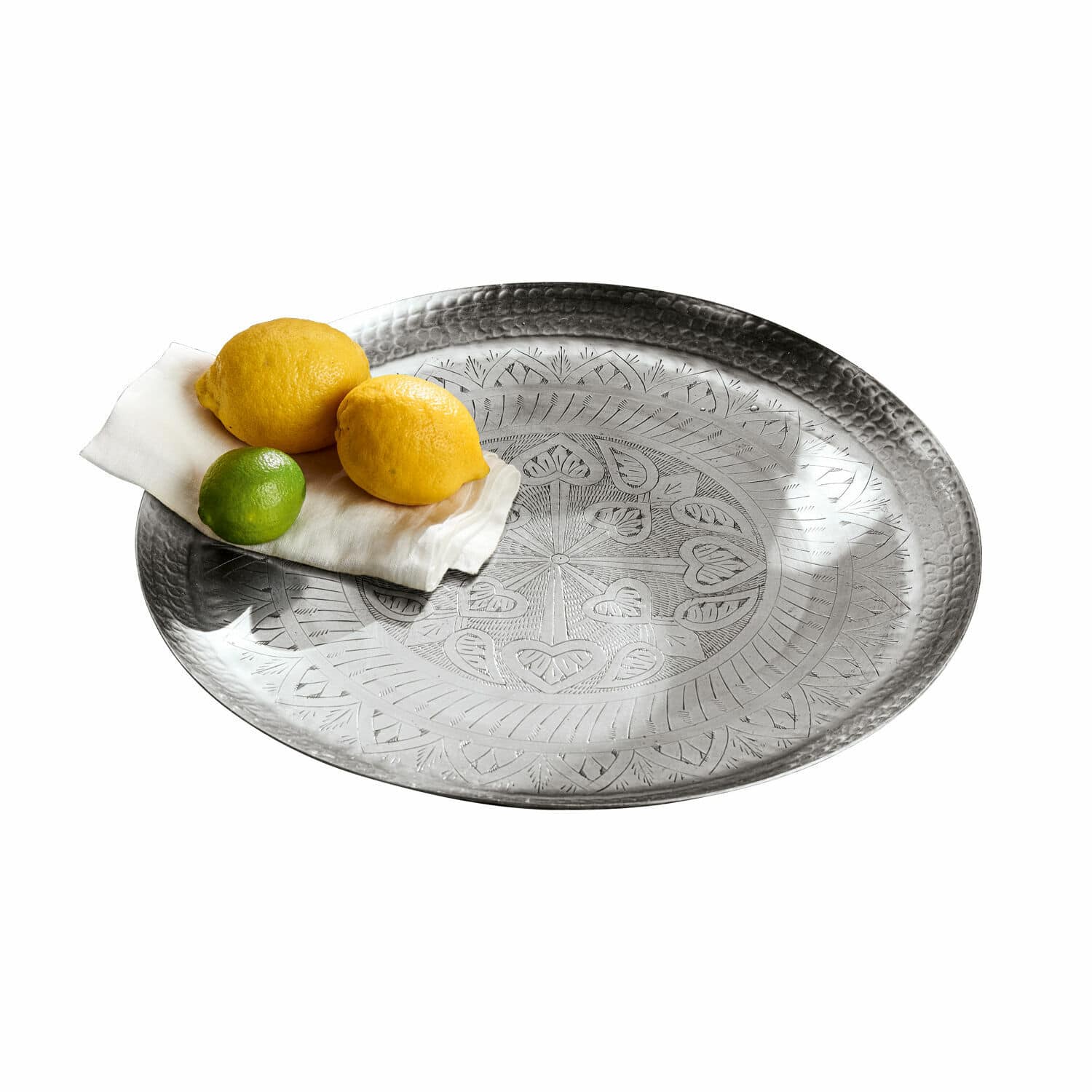 Plateau Moleur Plateau rond en métal argenté avec motif gravé, décoré de citrons et d’un citron vert sur une serviette blanche