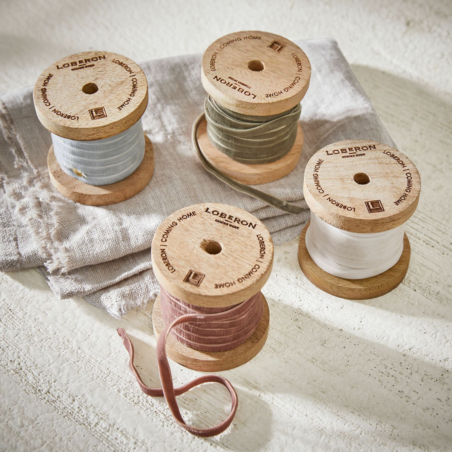 Lot de 4 rubans de velours Hilary Bobines en bois avec rubans en velours pastel posées sur tissu en lin, décoration intérieure élégante