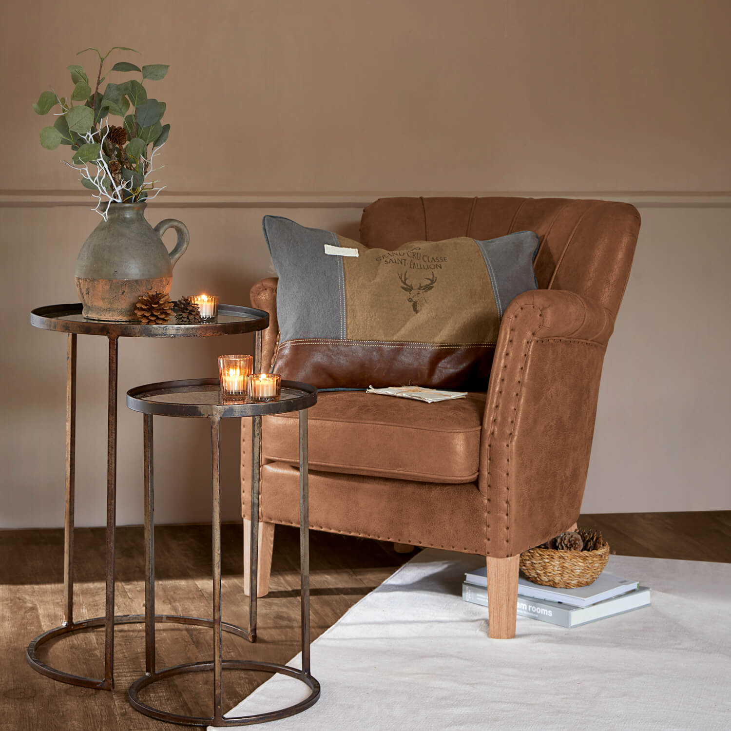 Bruine kunstleren fauteuil met decoratief kussen en metalen tafels met kaarsen en vaas