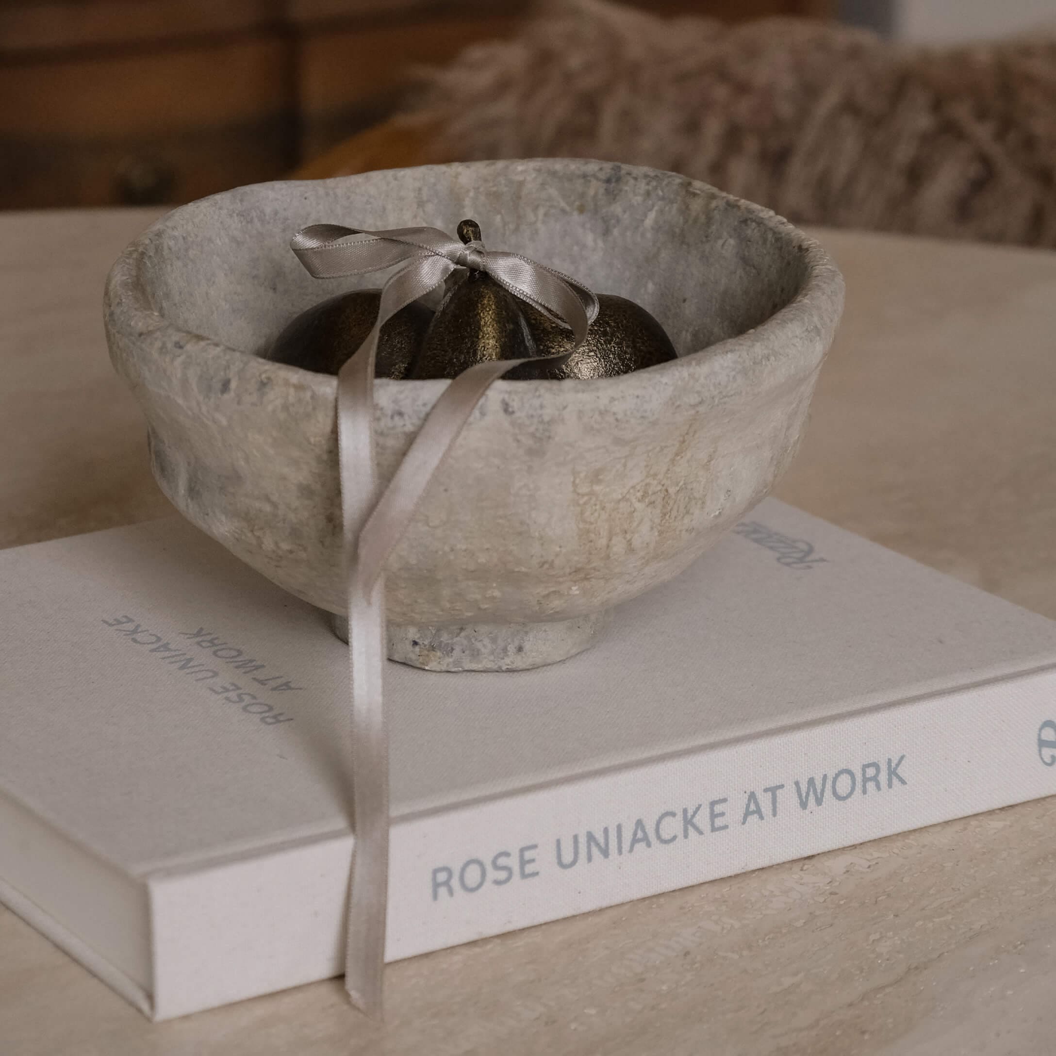 Bol décoratif en pierre grise avec ornement métallique et ruban posé sur un livre sur une table
