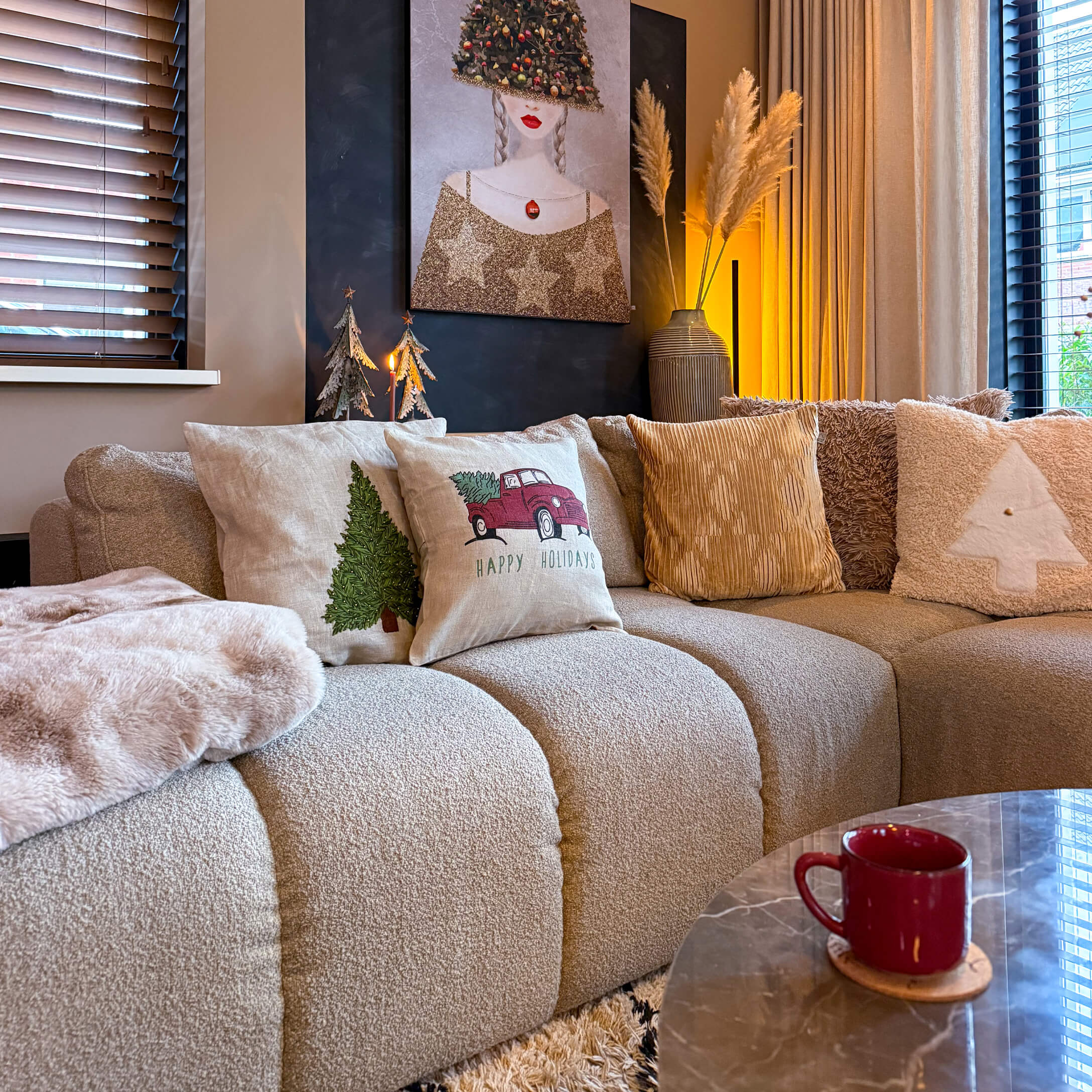 Canapé beige avec coussins décoratifs de Noël et tasse rouge sur table en marbre dans un salon cosy