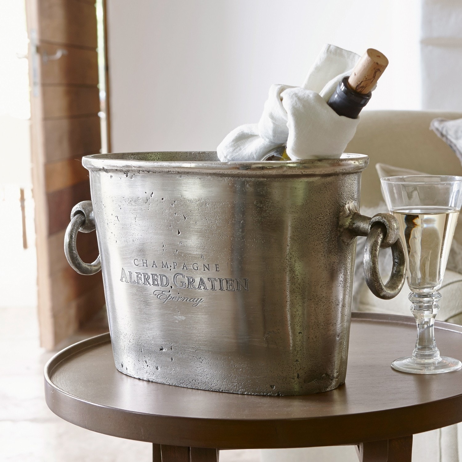 Champagnekoeler Alfred Zilverkleurige metalen champagnekoeler met handvatten en fles erin op ronde tafel