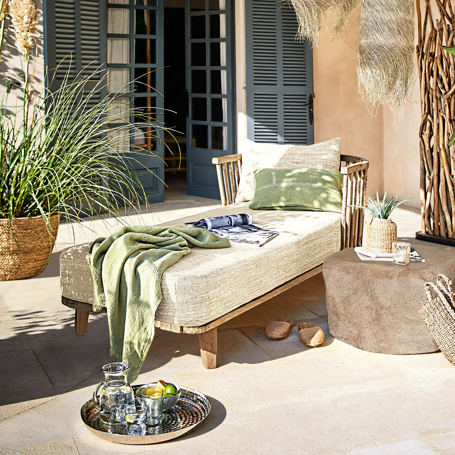 Méridienne Bellville Chaise longue en bois avec coussin beige et couverture verte sur terrasse décorée avec plateau de boissons