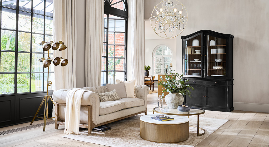 Canapé beige classique avec cadre en bois dans un salon lumineux avec vitrine noire et lampe sur pied