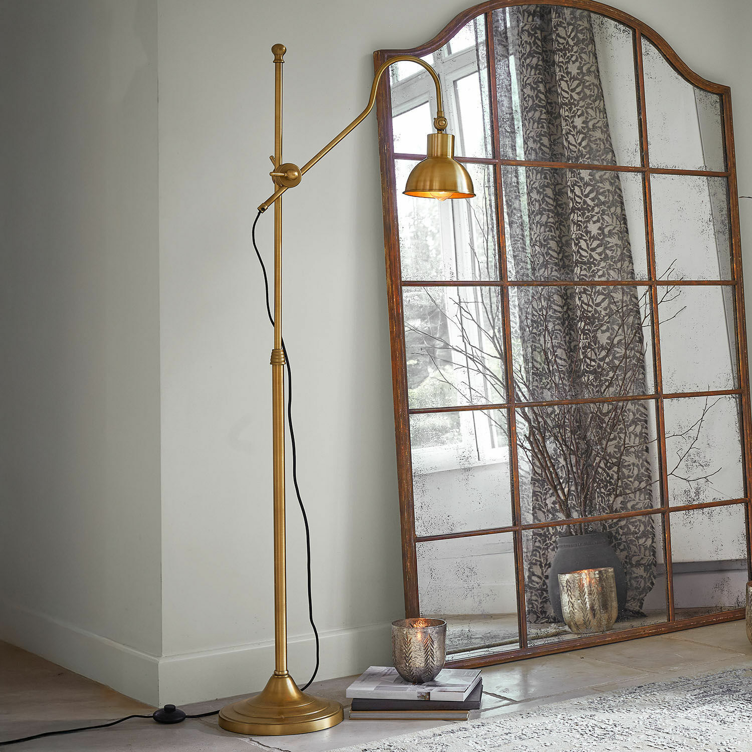 Vloerlamp Delacroille Gouden metalen vloerlamp met verstelbare arm naast een grote vintage spiegel