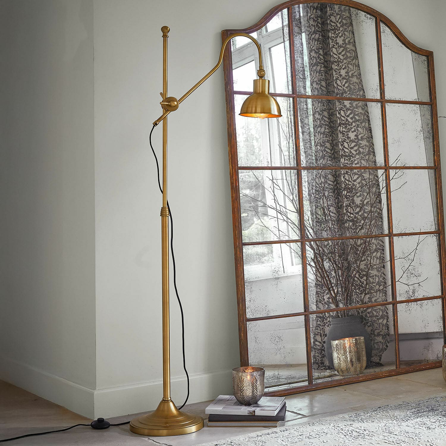 Vloerlamp Delacroille Gouden metalen vloerlamp met verstelbare arm naast een grote vintage spiegel