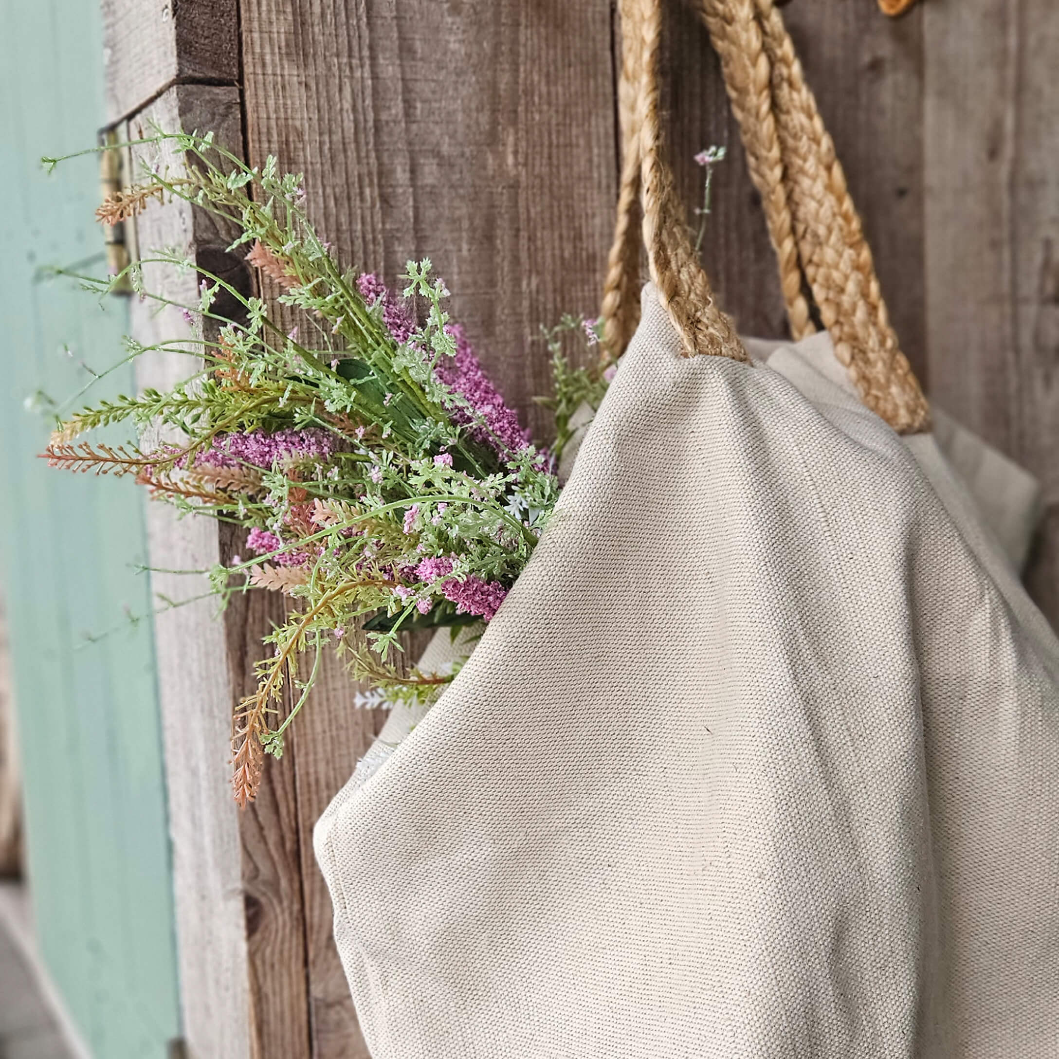 Sac beige en tissu naturel avec poignées tressées et fleurs sur fond en bois rustique