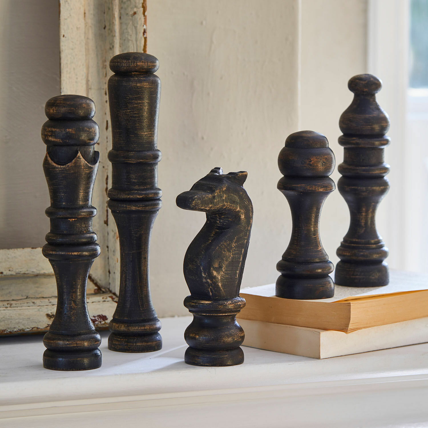 Deco-object set van 5 Guillemineau Decoratieve zwarte houten schaakstukken met verouderde look op een plank naast boeken.