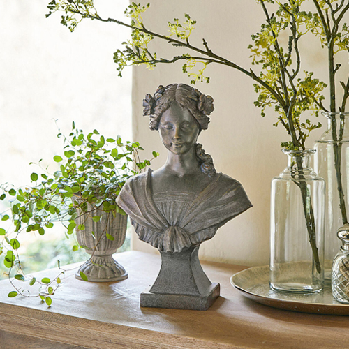 Buste féminin en pierre grise avec fleurs dans les cheveux sur une table en bois décorée de plantes