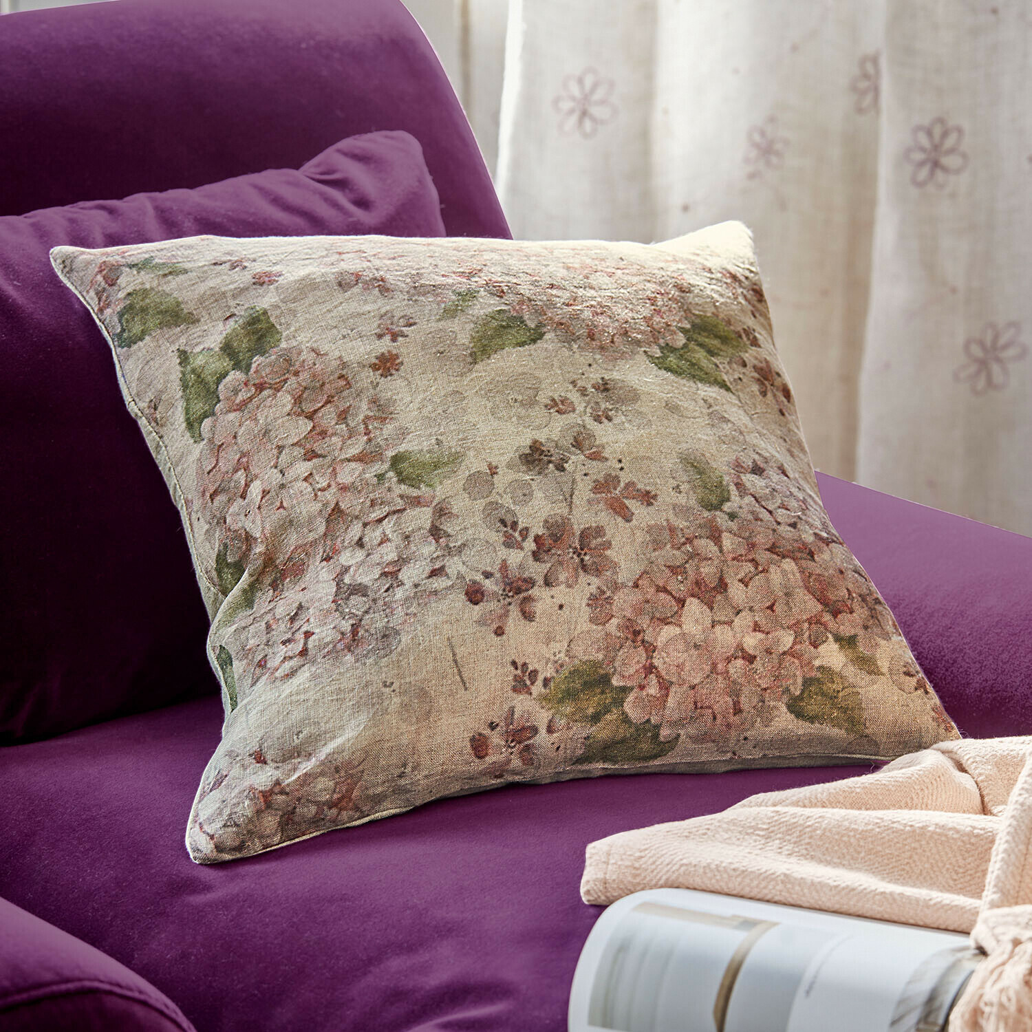 Housse de coussin Amélorie Coussin décoratif en lin à motif floral posé sur un canapé violet, accessoire cosy pour la maison