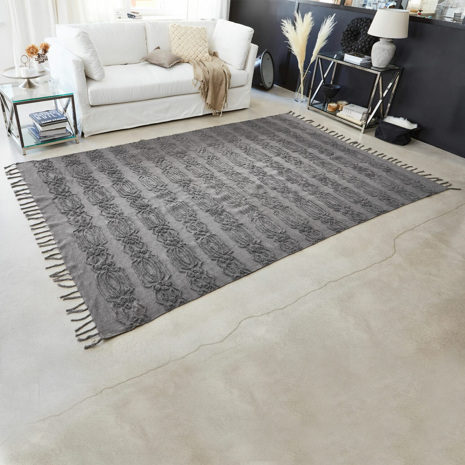Tapis gris en coton avec motif décoratif et franges dans un salon moderne avec canapé blanc
