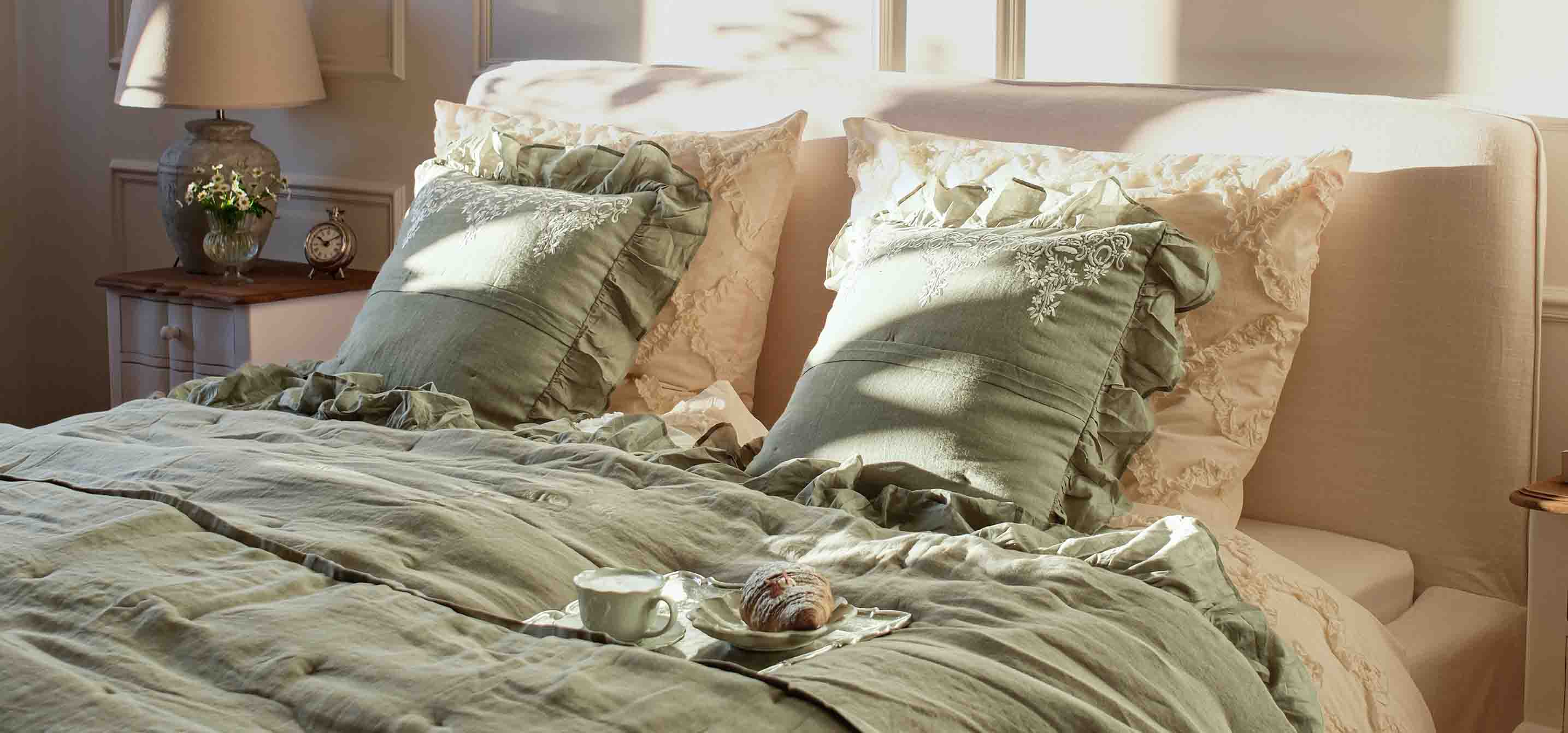 Groen beddengoed en kussens met ruches op bed in lichte slaapkamer met lamp en klok