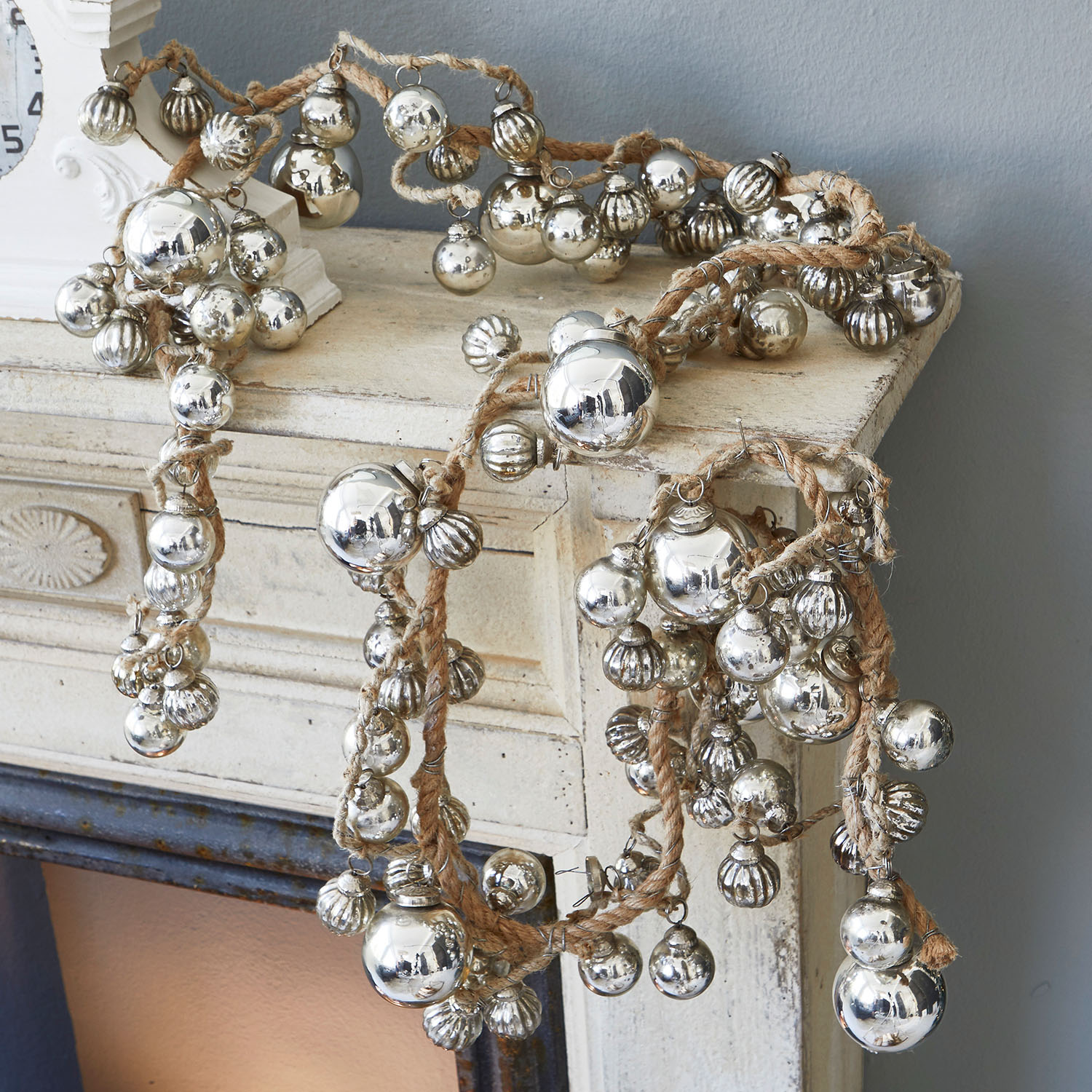 Guirlande van juten touw met zilverkleurige metalen decoratieve ballen op een schoorsteenmantel