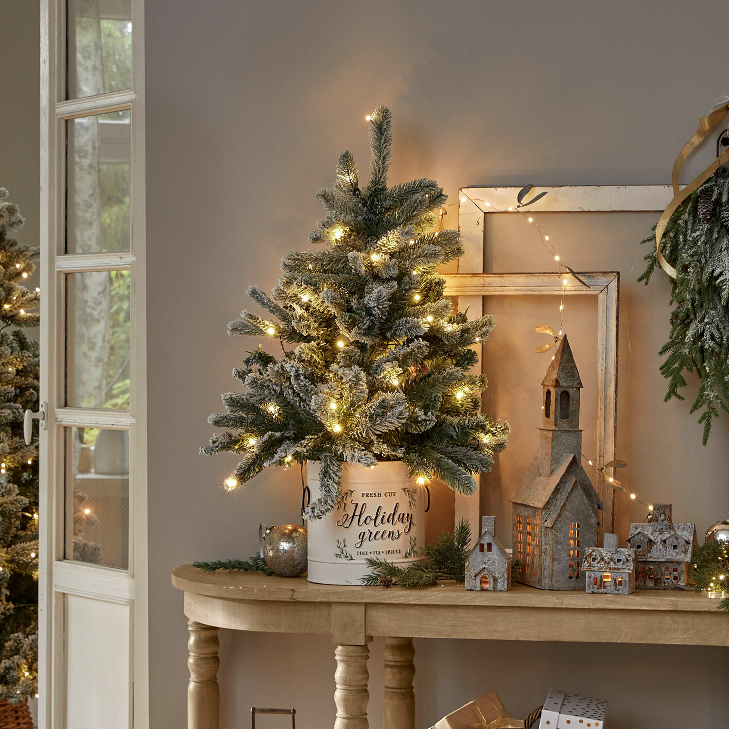 Kerstboom Mannier Kerstdecoratie met verlichte kunstkerstboom in witte metalen emmer op houten tafel