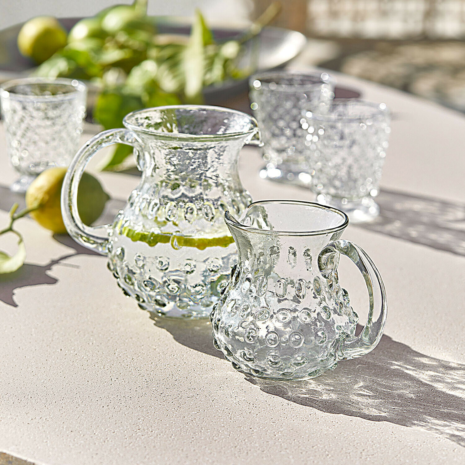 Carafe et pichet en verre texturé sur table claire, parfaits pour servir des boissons fraîches