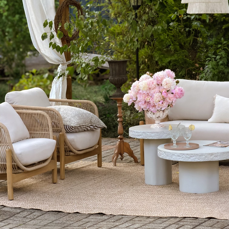 Tuinmeubelset met lichte kussens, rotan stoelen en betonnen tafels op jute vloerkleed buiten