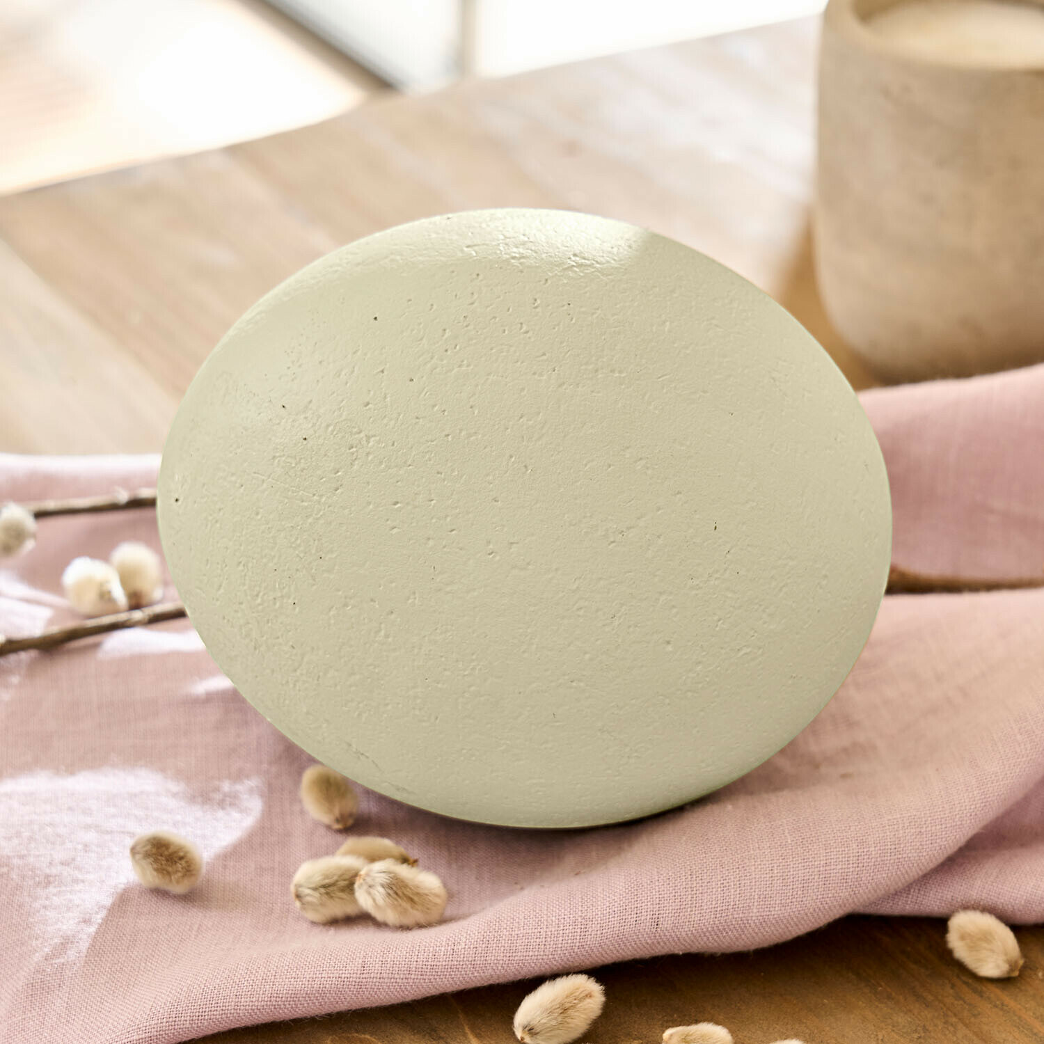 Œuf décoratif Fauverine Œuf décoratif en céramique mate couleur crème posé sur un tissu rose pour décoration intérieure