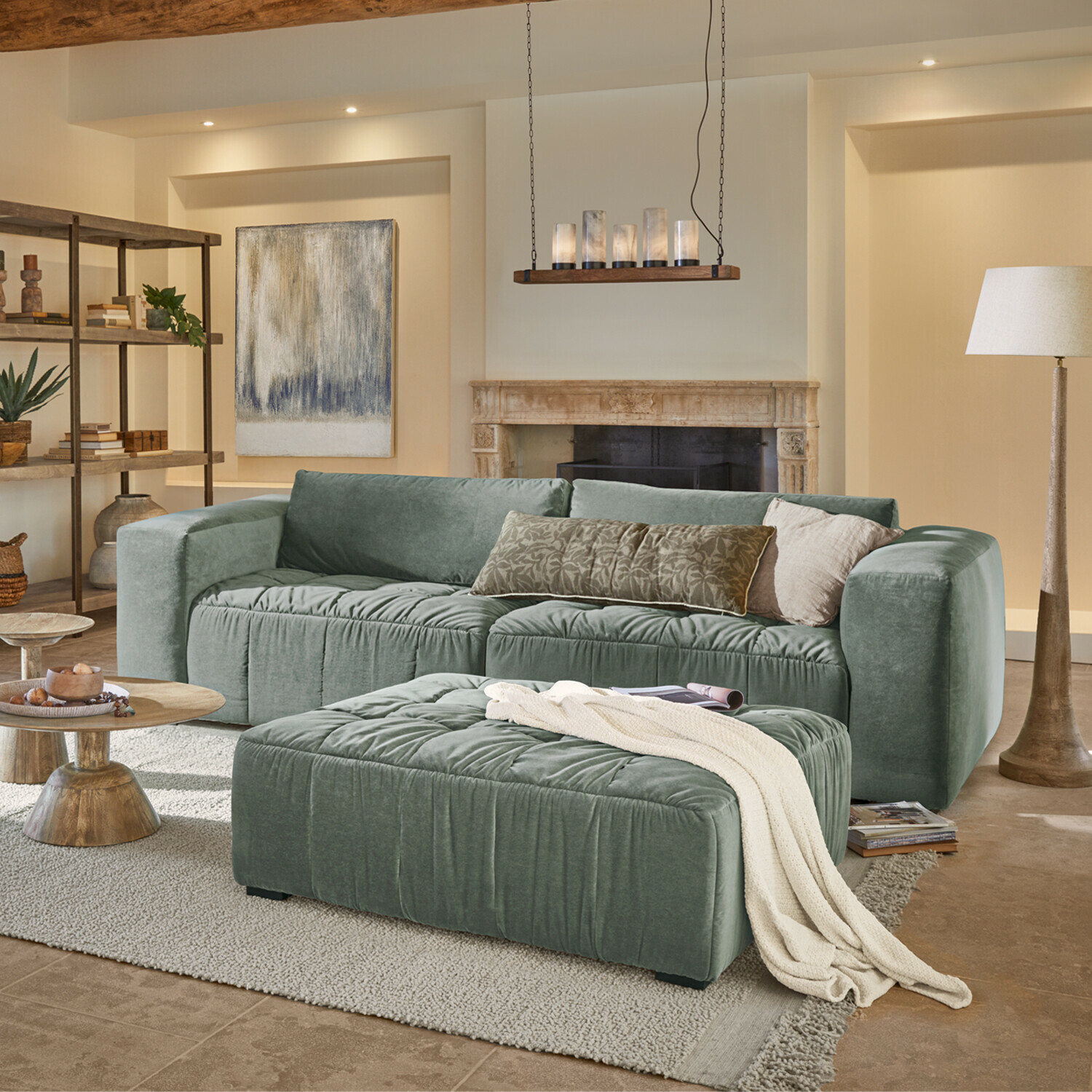 Canapé Ottolline Canapé vert en velours avec coussins et pouf dans un salon chaleureux avec cheminée et lampe sur pied